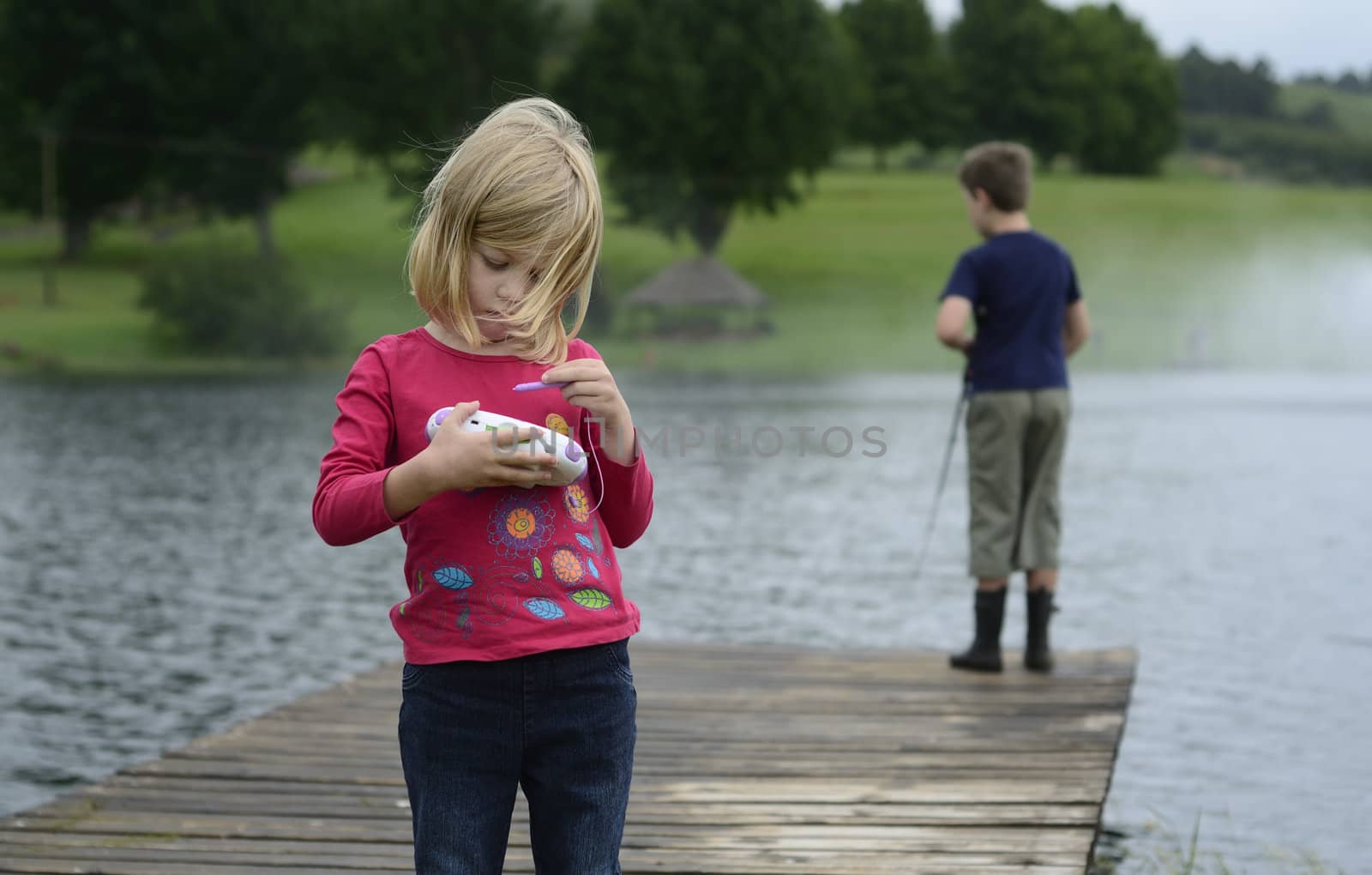 Young girl playing computer game in nature by alistaircotton