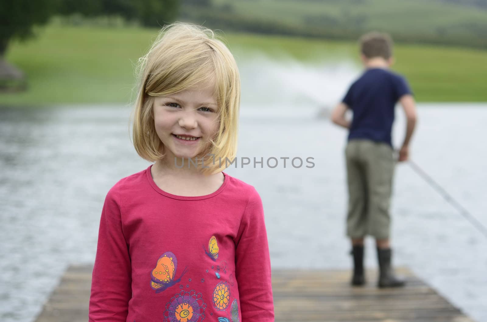 Young girl and boy fishing on wooden pier by alistaircotton