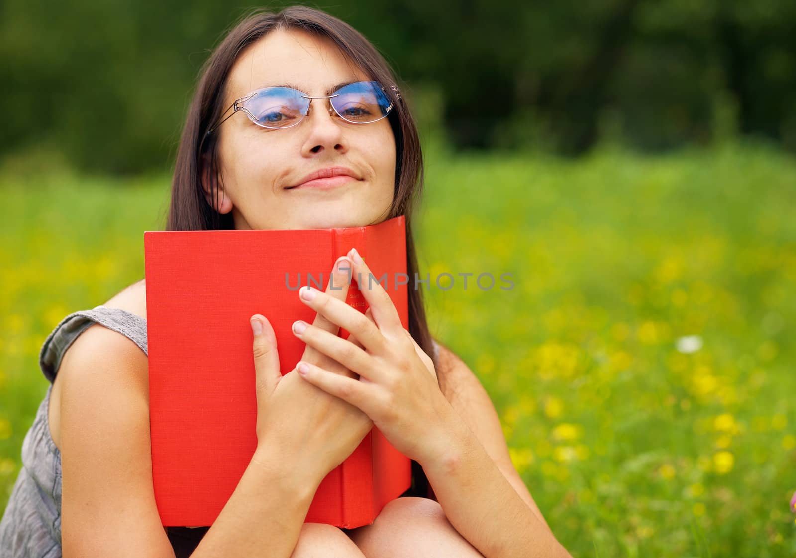 Closeup portrait of a young  female with a book  on a green meadow