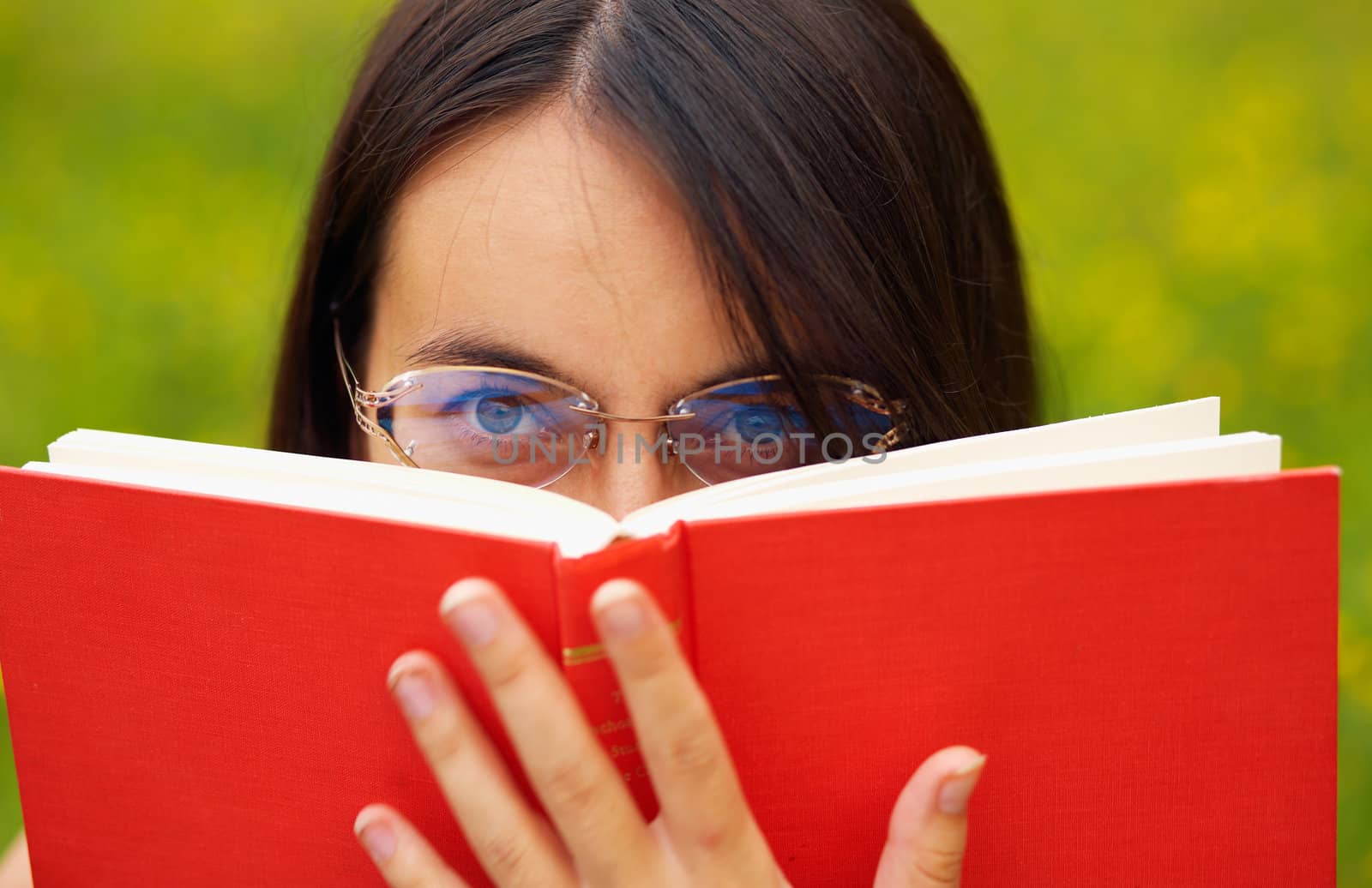 Closeup portrait of a young  female with a book  on a green meadow