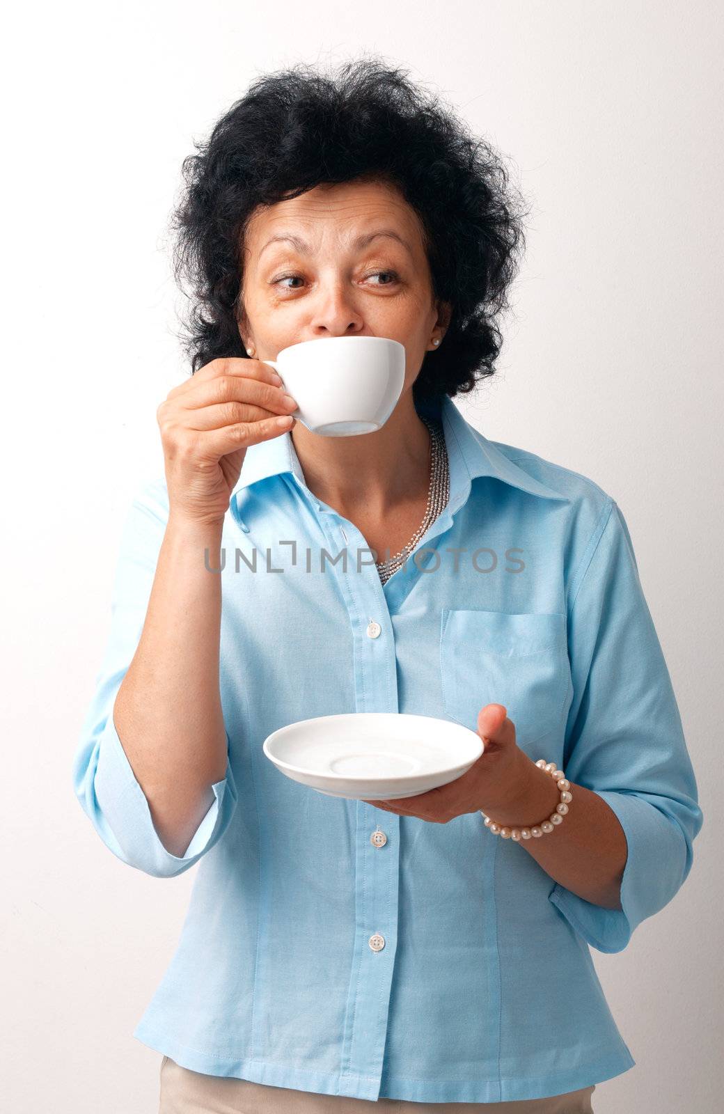 Portrait of an elder woman drinking from a cup and holding a saucer.