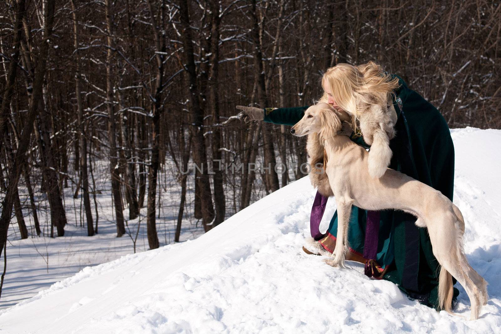 A blonde girl and a standing white saluki on snow
