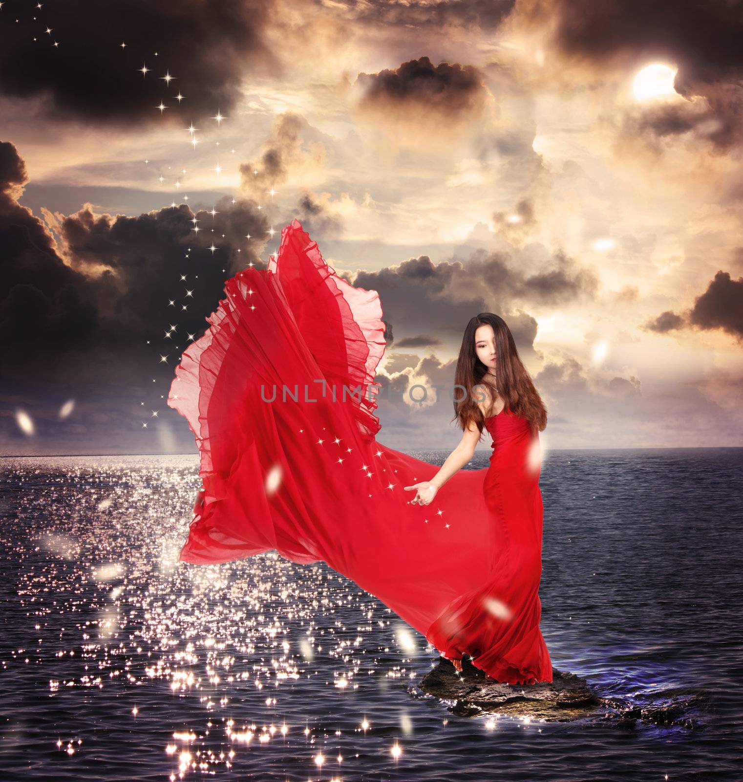 Beautiful Girl in Red Dress Standing on Ocean Rocks 