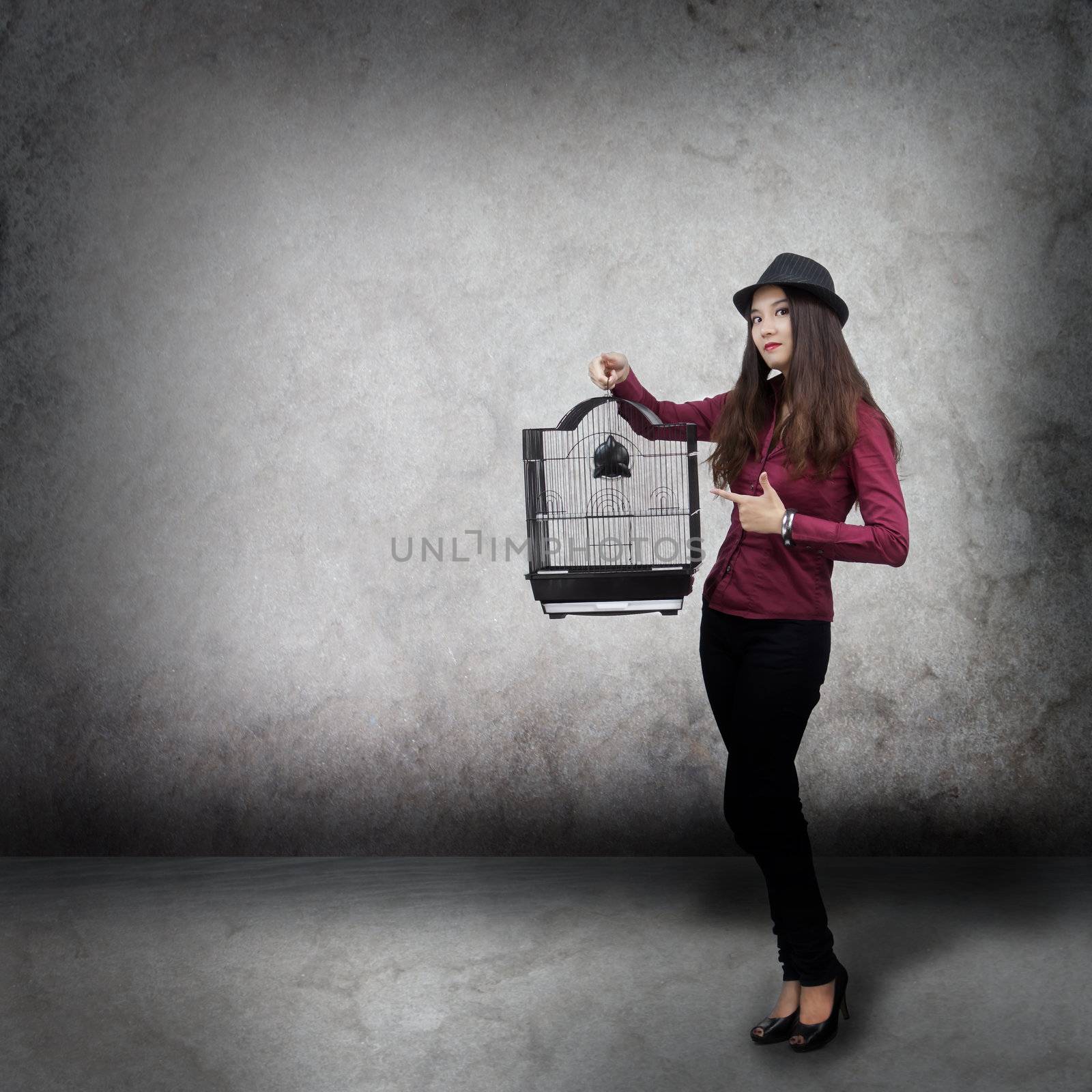 Young woman holding a bird cage on gray stone background