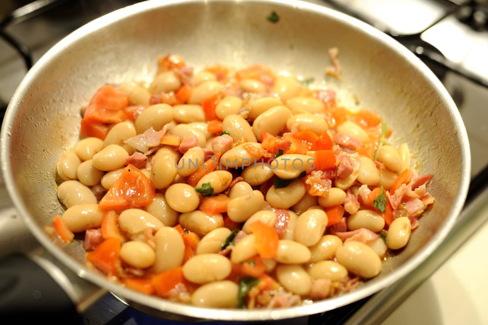 The making of a dish of beans with bacon and tomatos