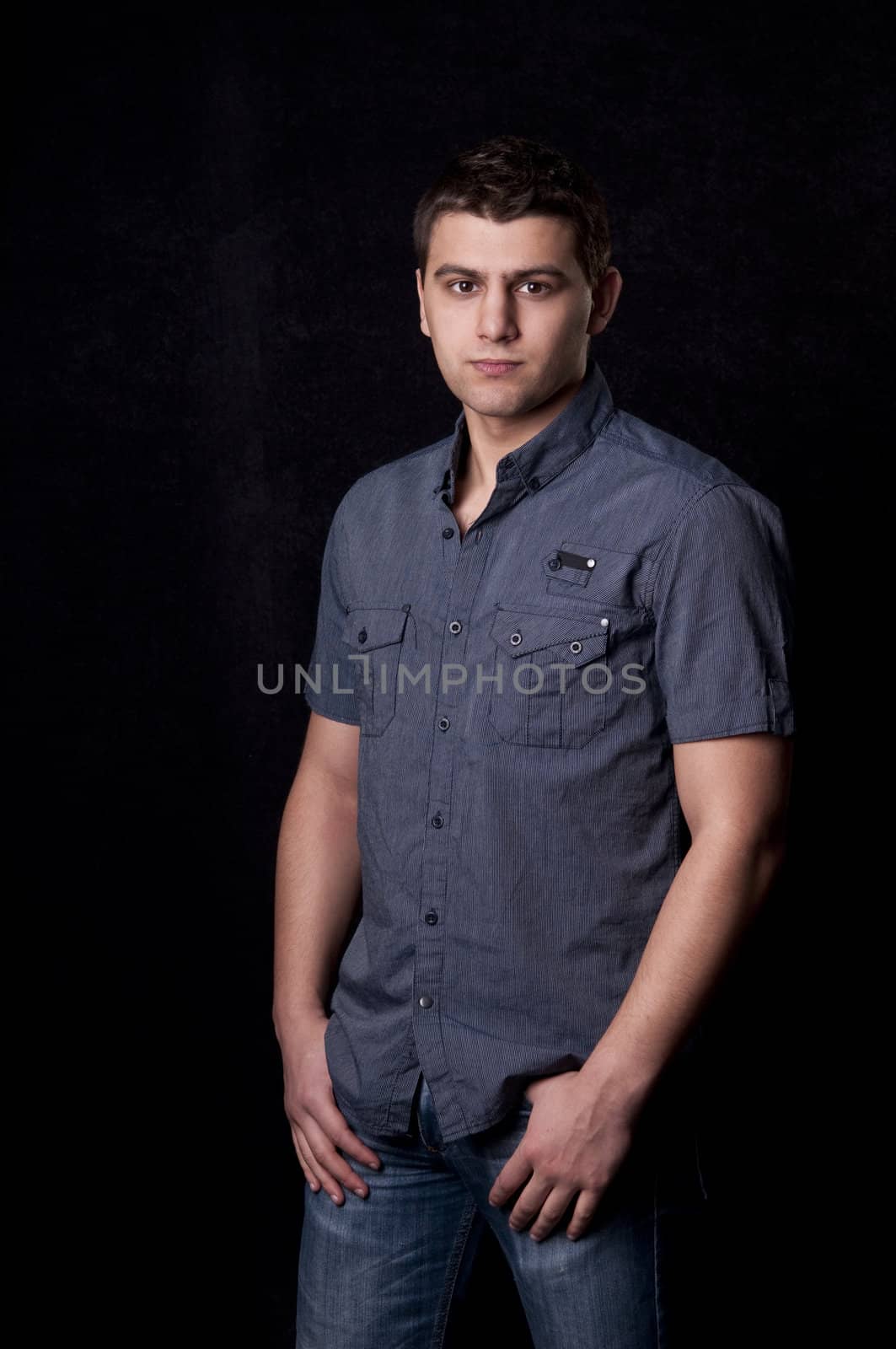 Serious casual young man in jeans on black background