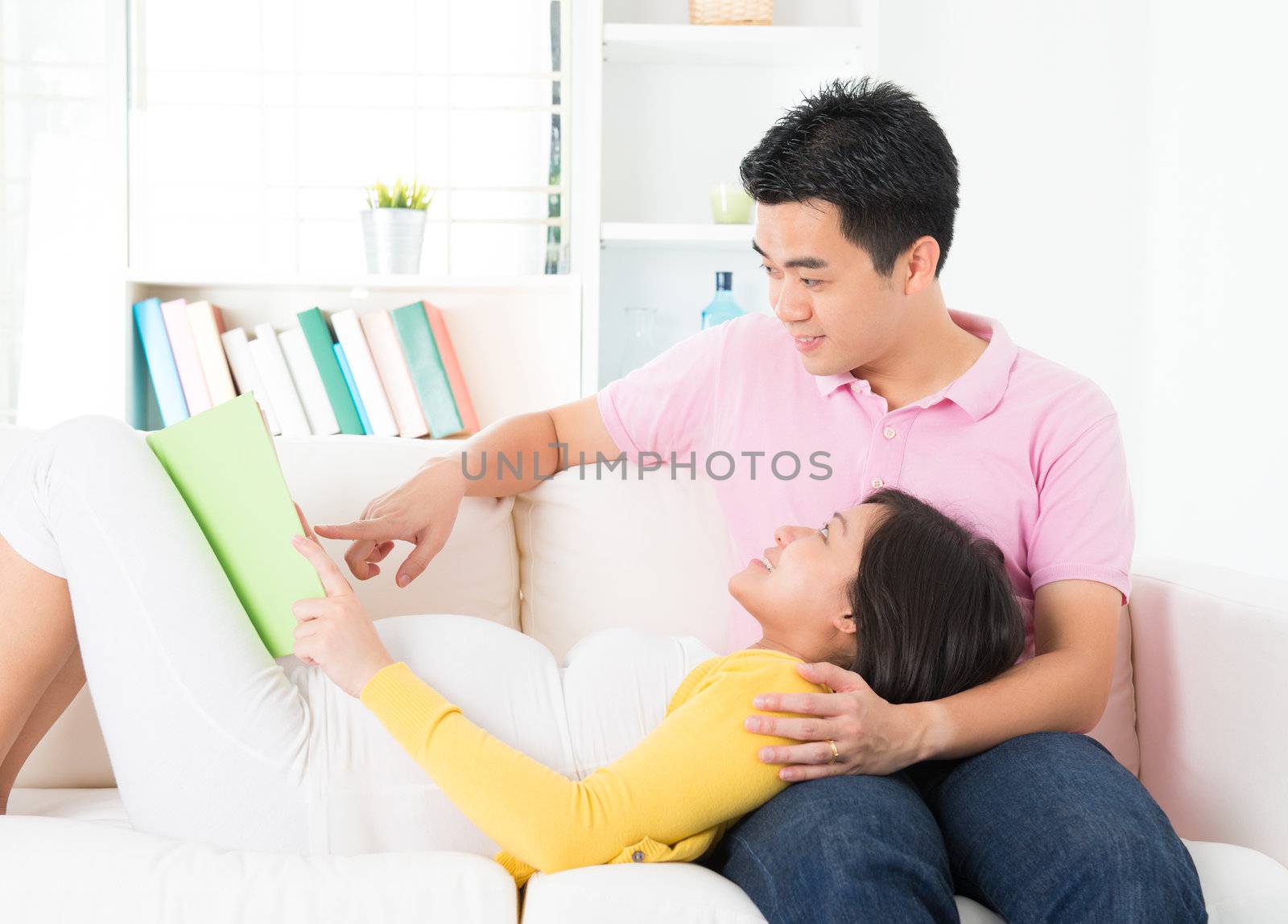 Asian pregnant woman reading book together with husband