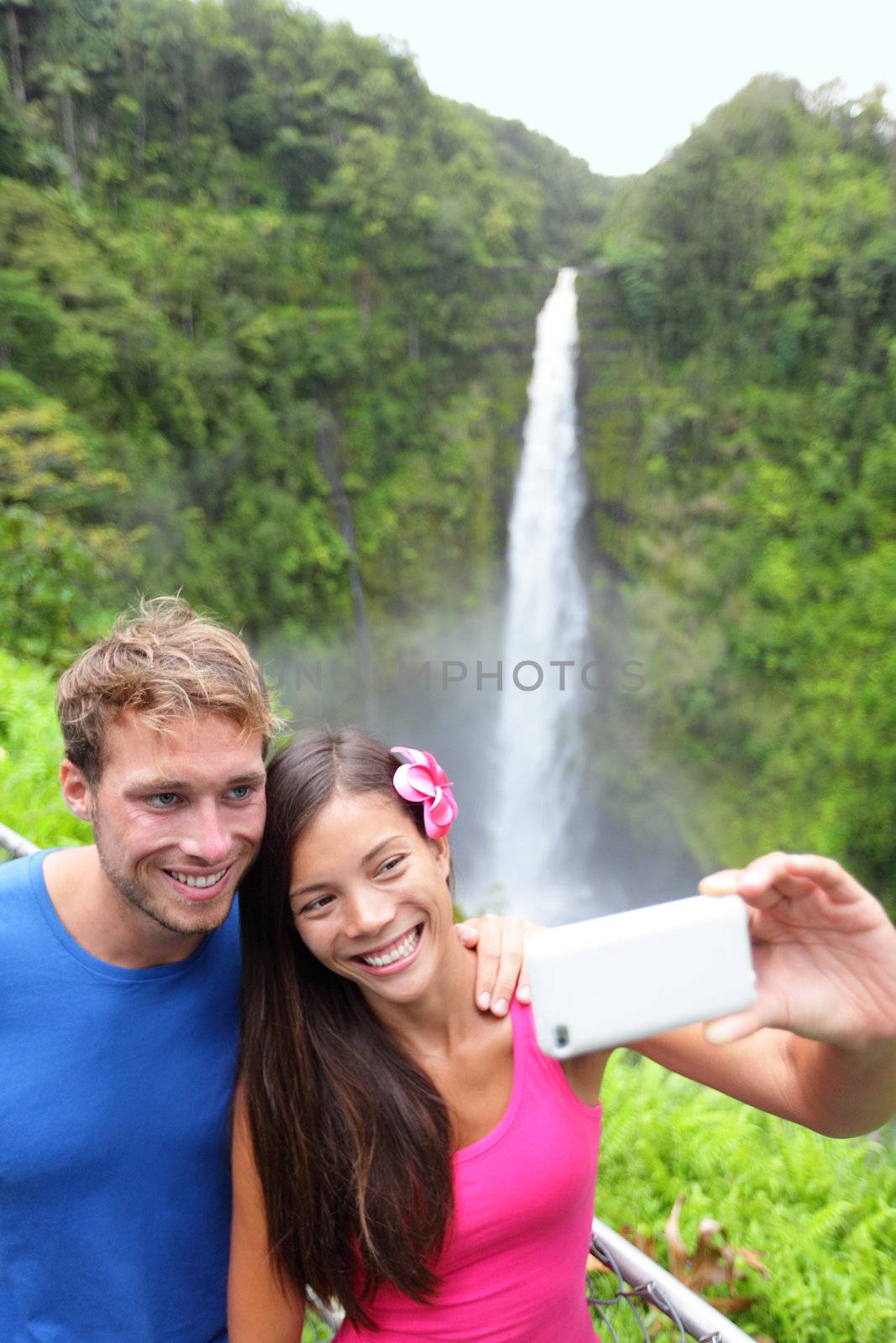 Tourists couple taking self portrait photo on Hawaii with camera phone on Hawaii, Big Islands, Akaka Falls. Happy cheerful young multiethnic couple on travel.