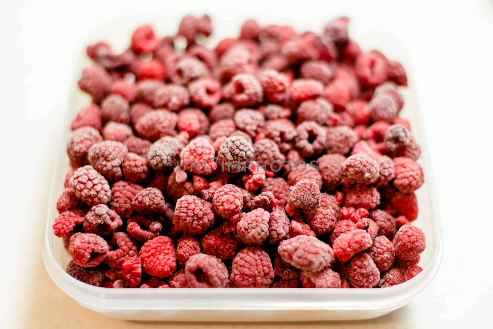 frozen raspberries in a plastic box on white background
