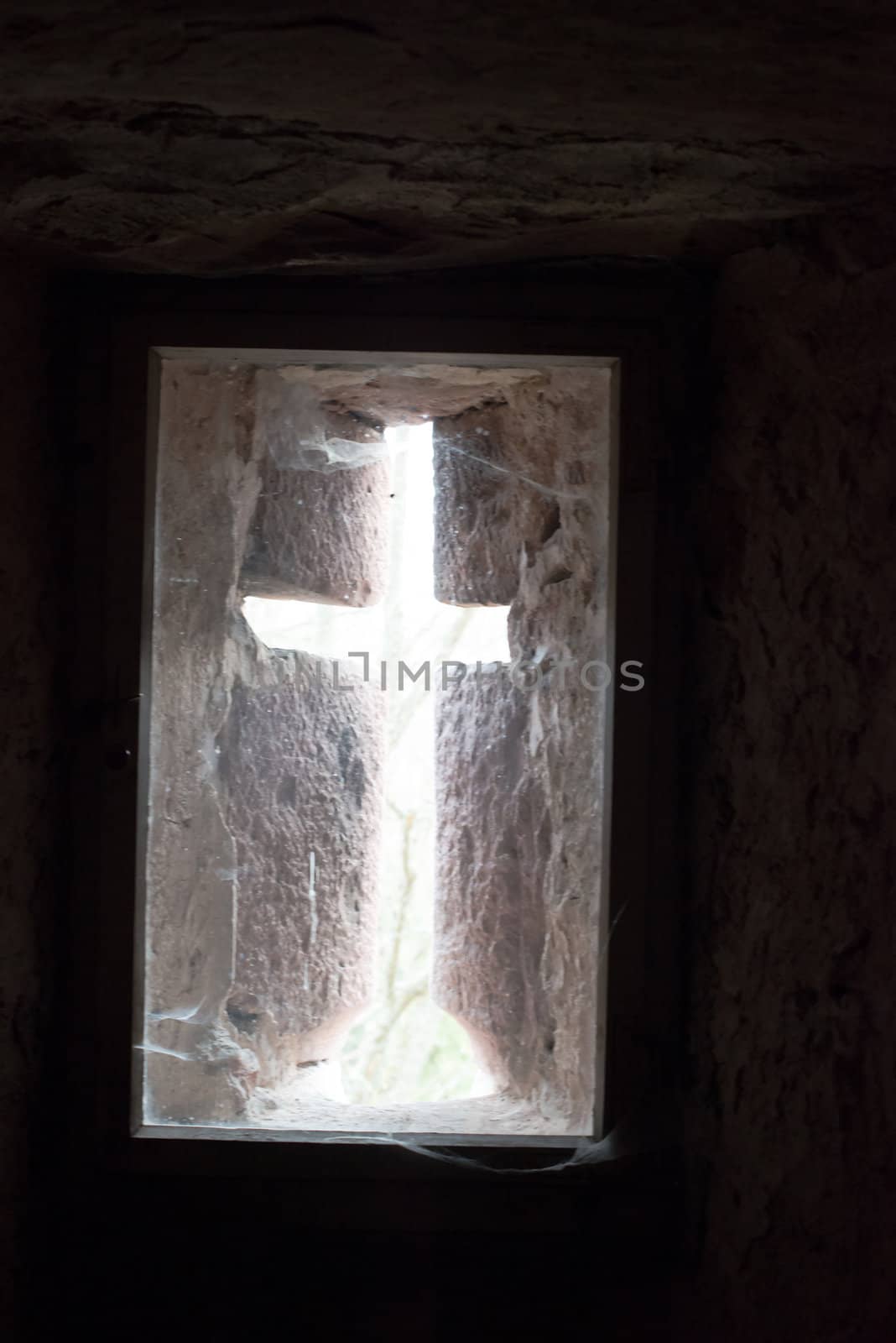 Contrasting light shines in the shape of a cross through the window of an old castle