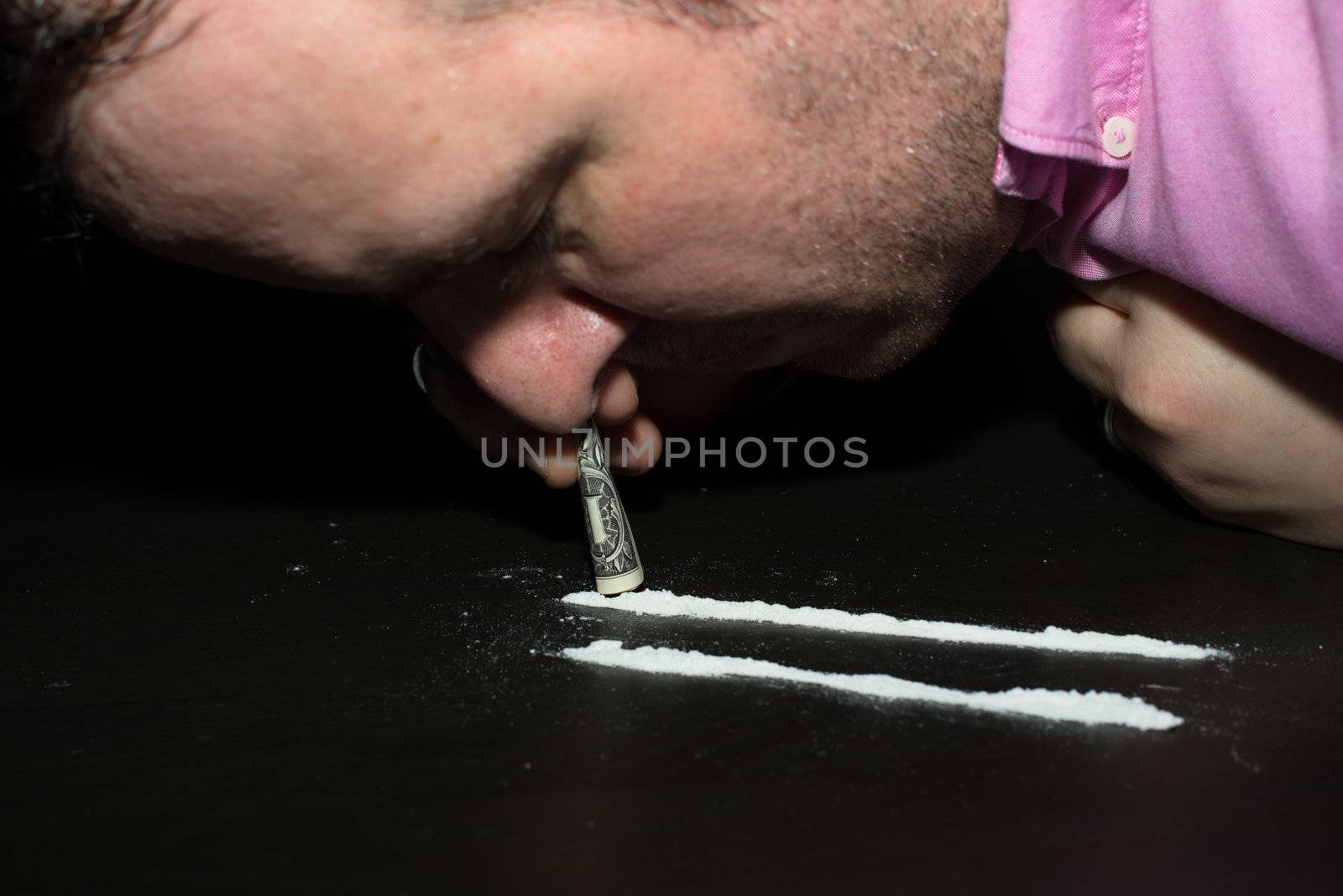 Drug Abuse: Young man sniffing cocaine using a Dollar note