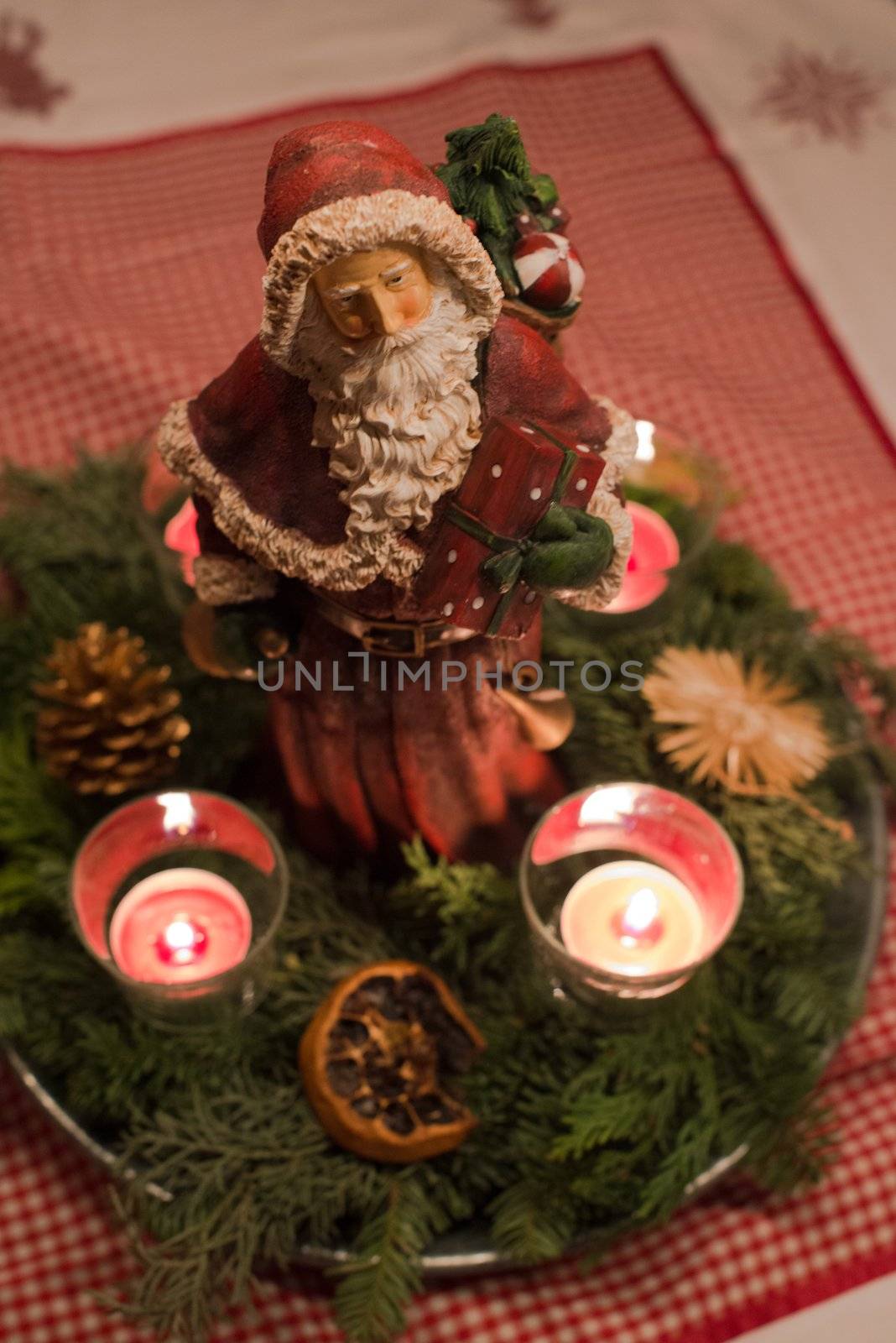 Advent wreath with burning red candles and Santa Claus figure in the centre on decorative table cloth
