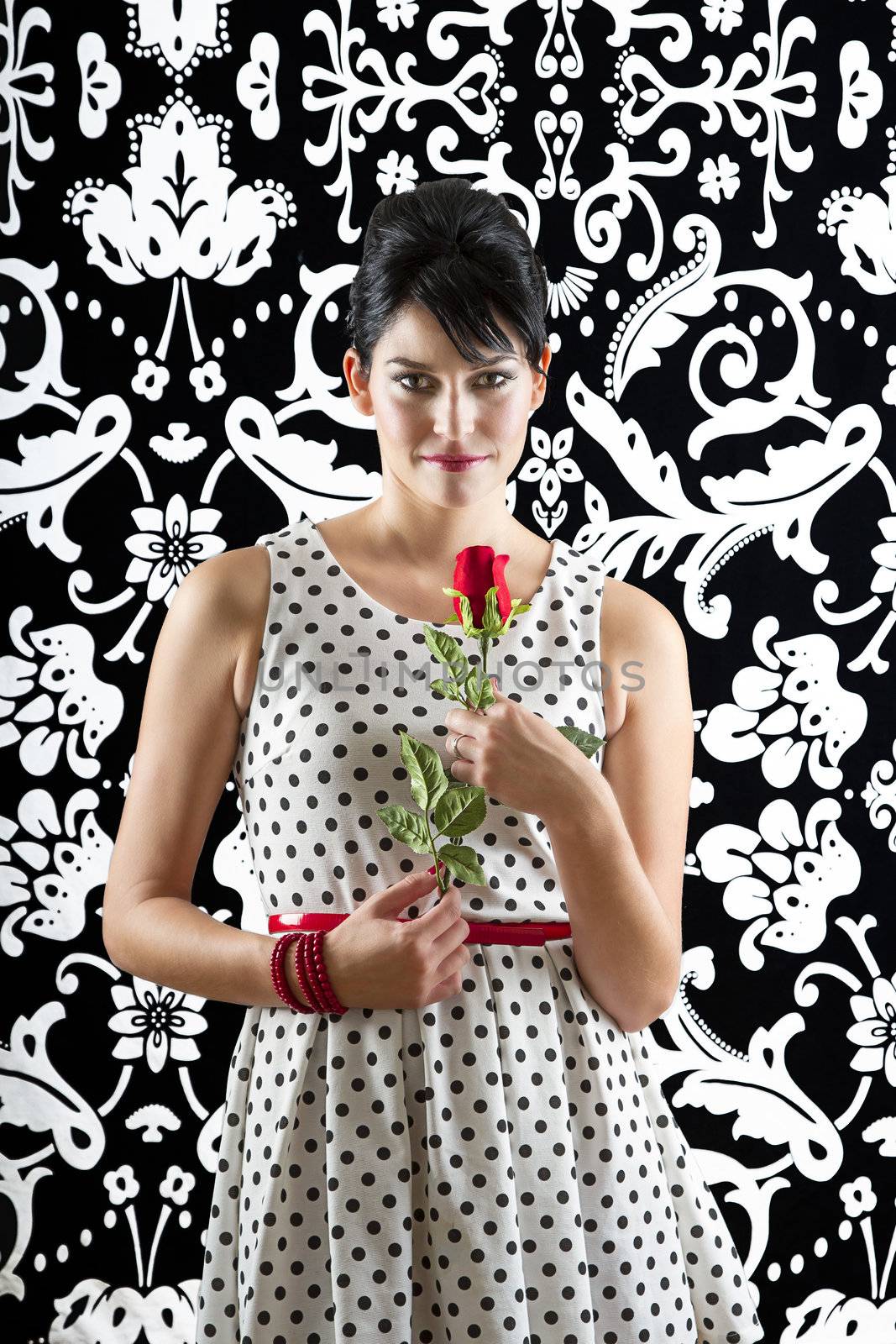 young woman in front of a black and white textured background with 60's inspired style holding a rose