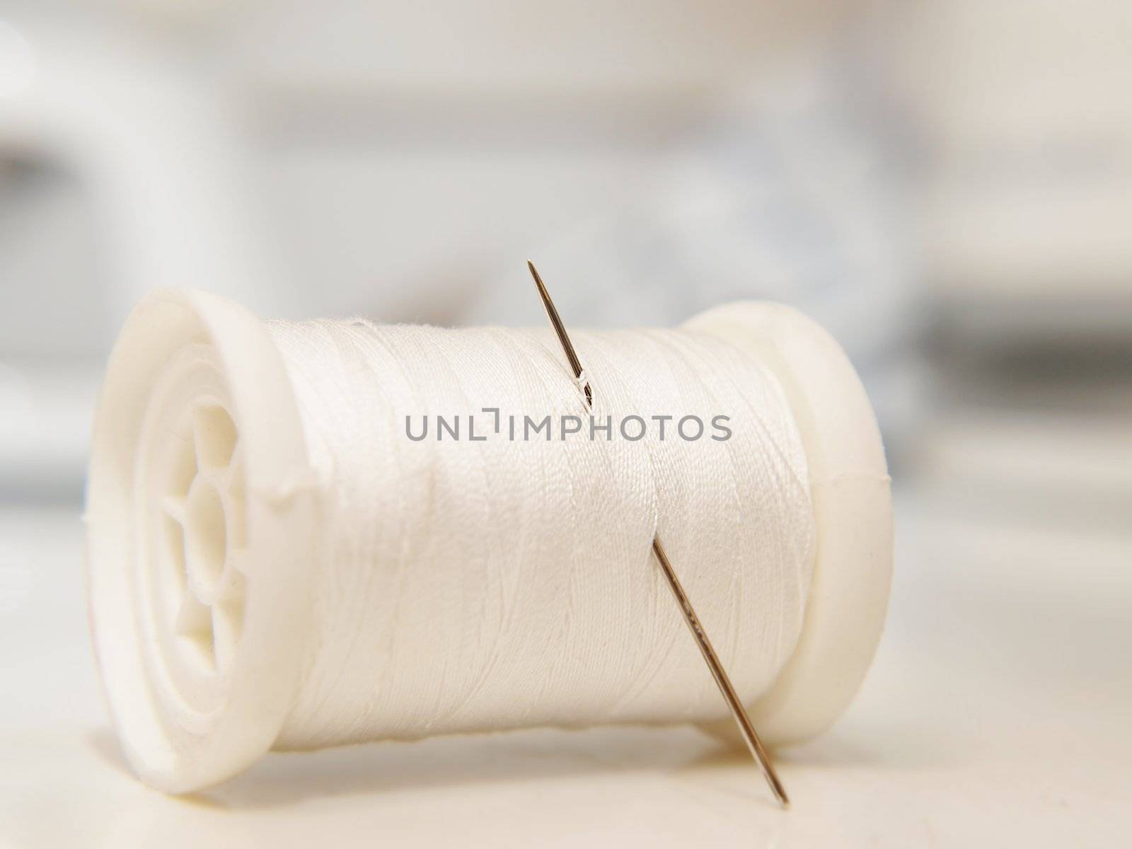 White thread on spool, laying down, with a needle