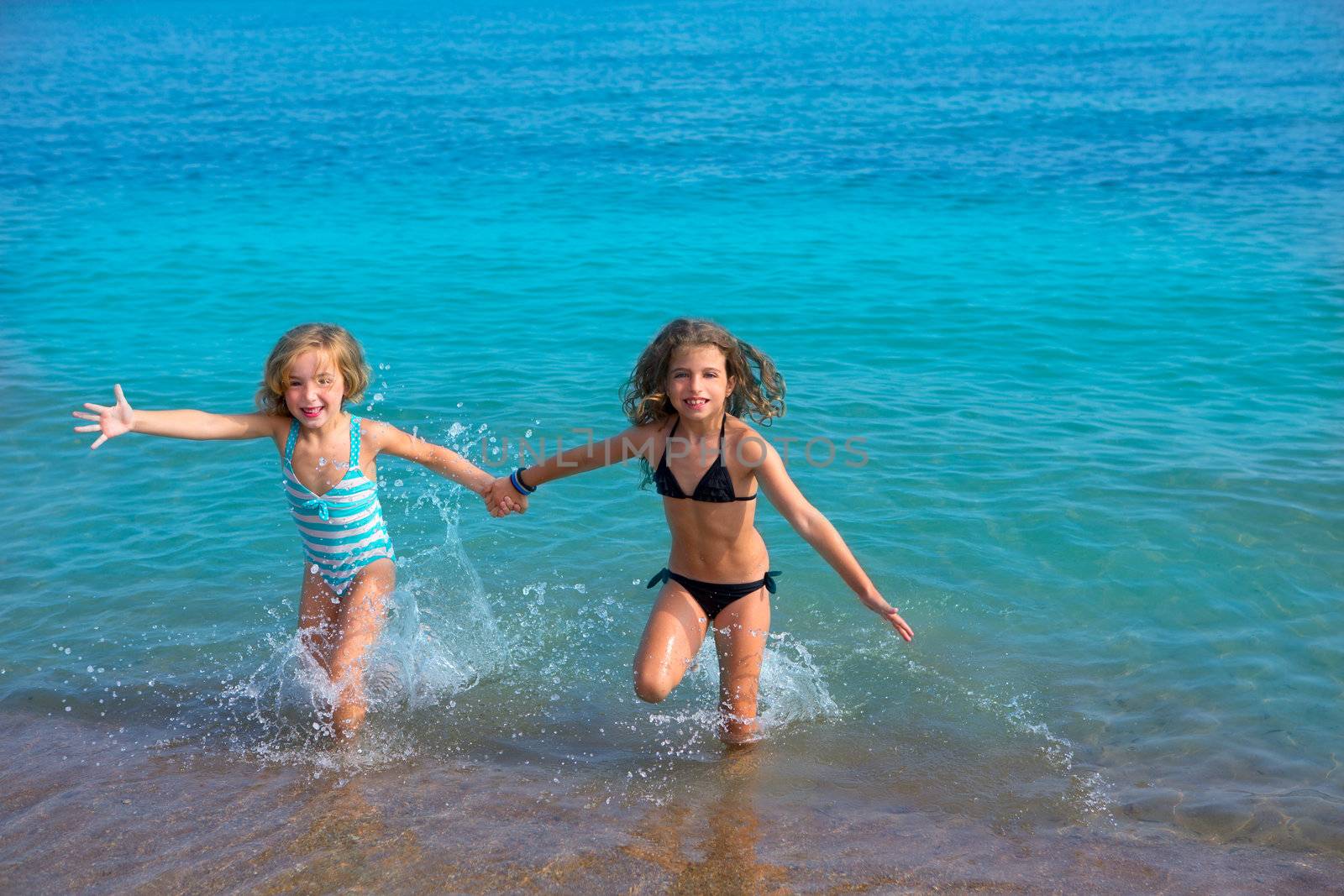 children girls friends running together in the beach shore by lunamarina