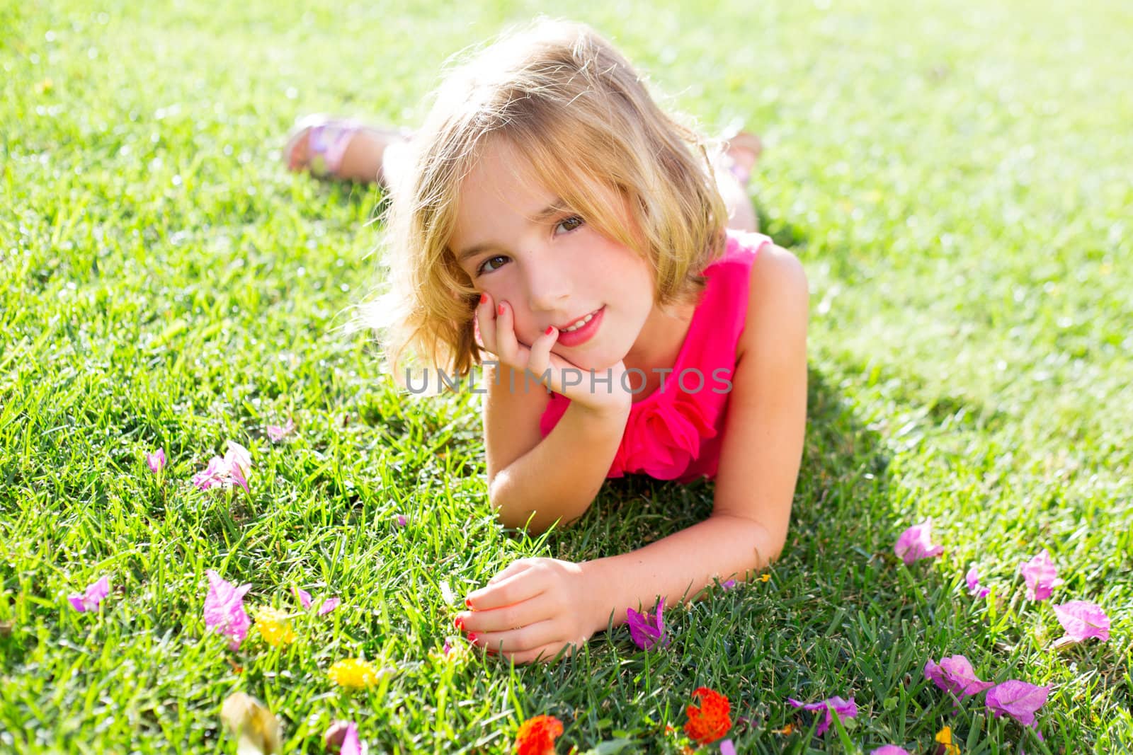 blond kid girl lying relaxed in garden grass with flowers smiling