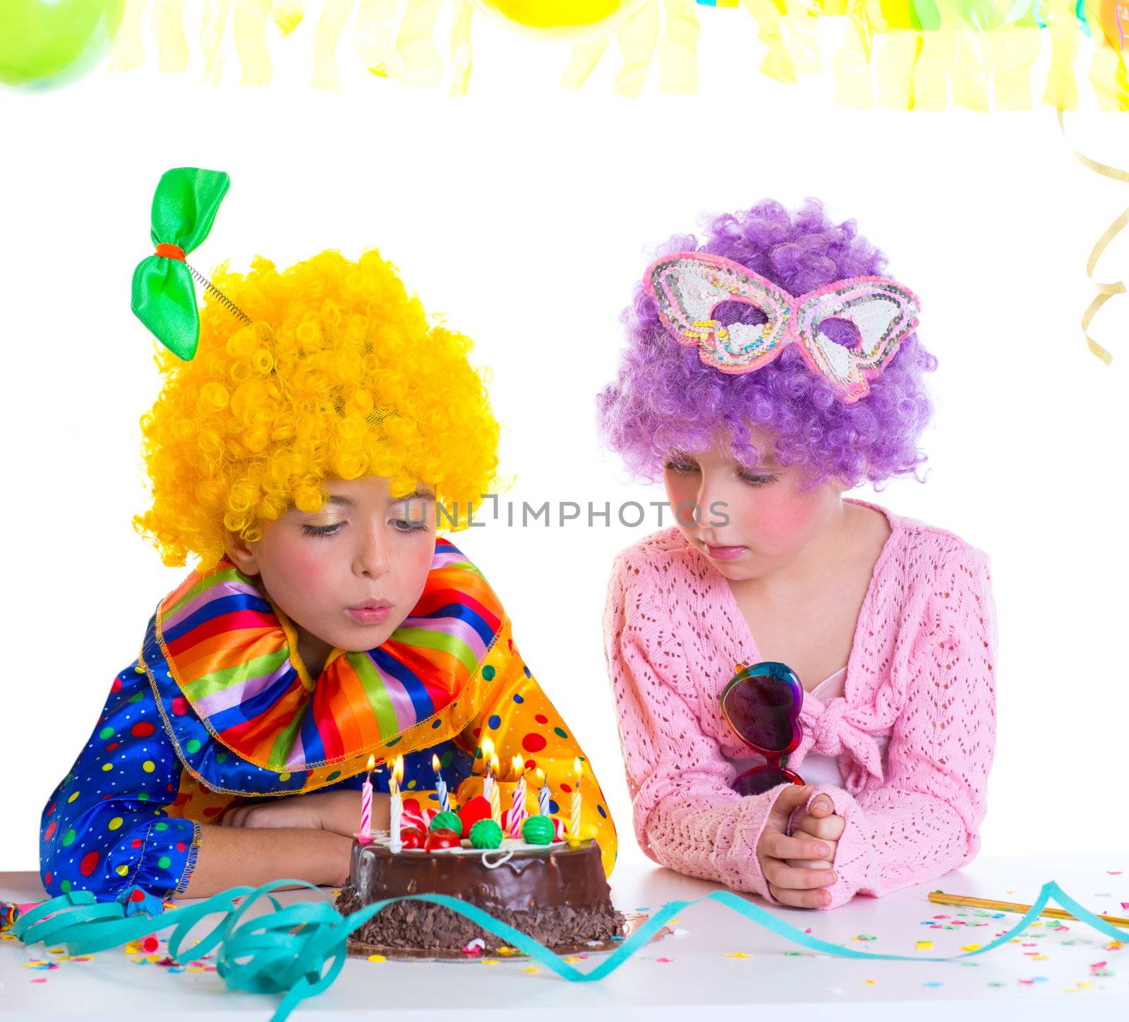 Children happy birthday party with clown wigs blowing chocolate cake candles
