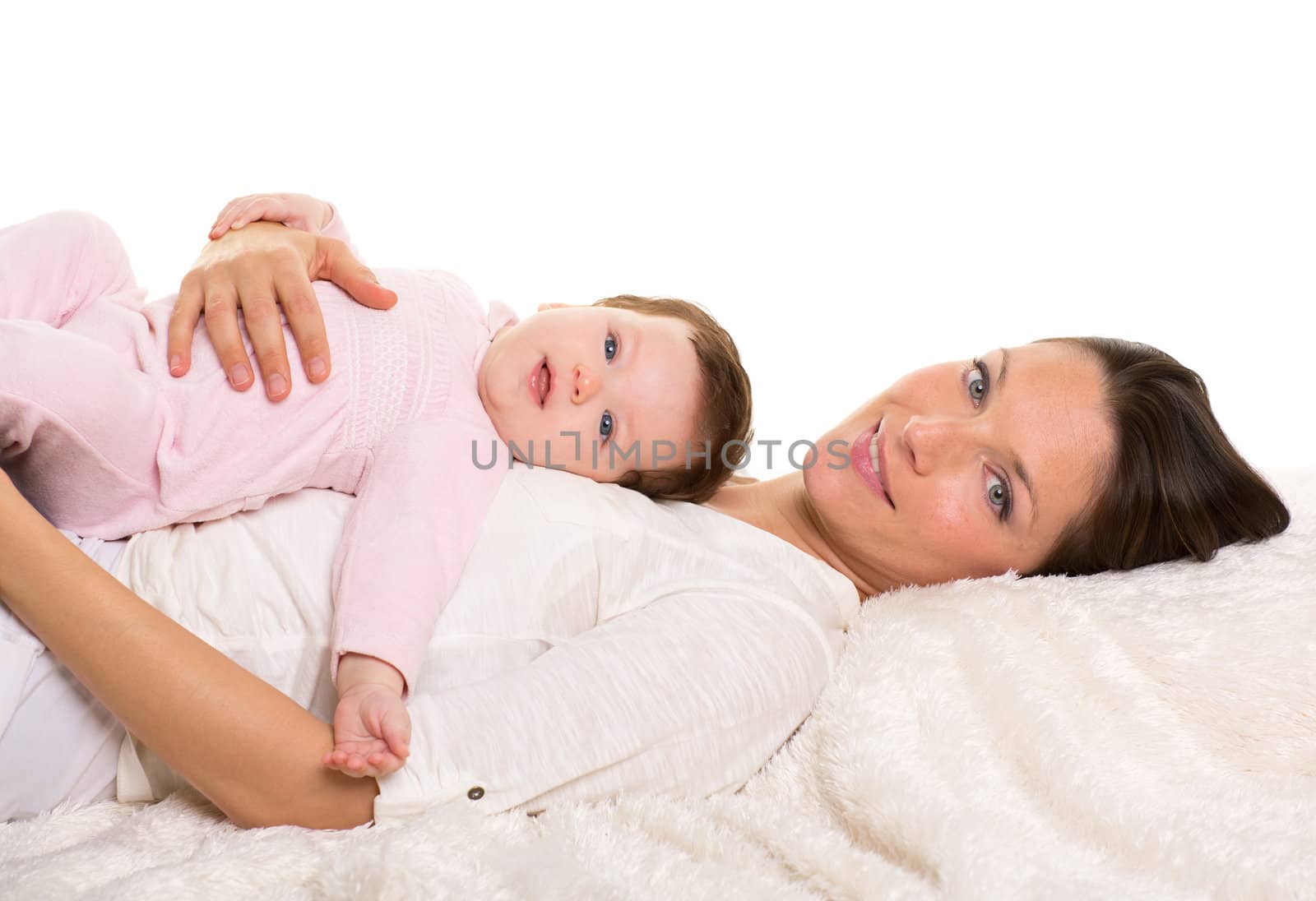 Baby girl and mother lying happy together on white fur blanket