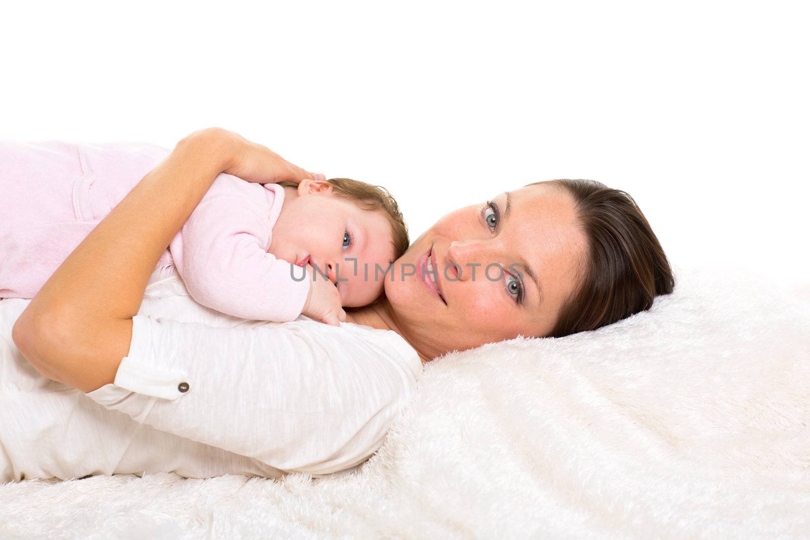 Baby girl and mother lying happy together on white fur blanket