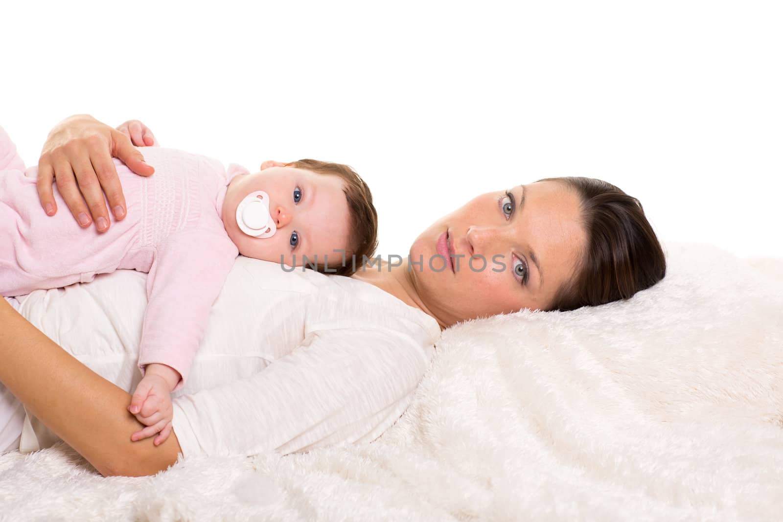 Baby girl and mother lying happy together on white fur with pacifier
