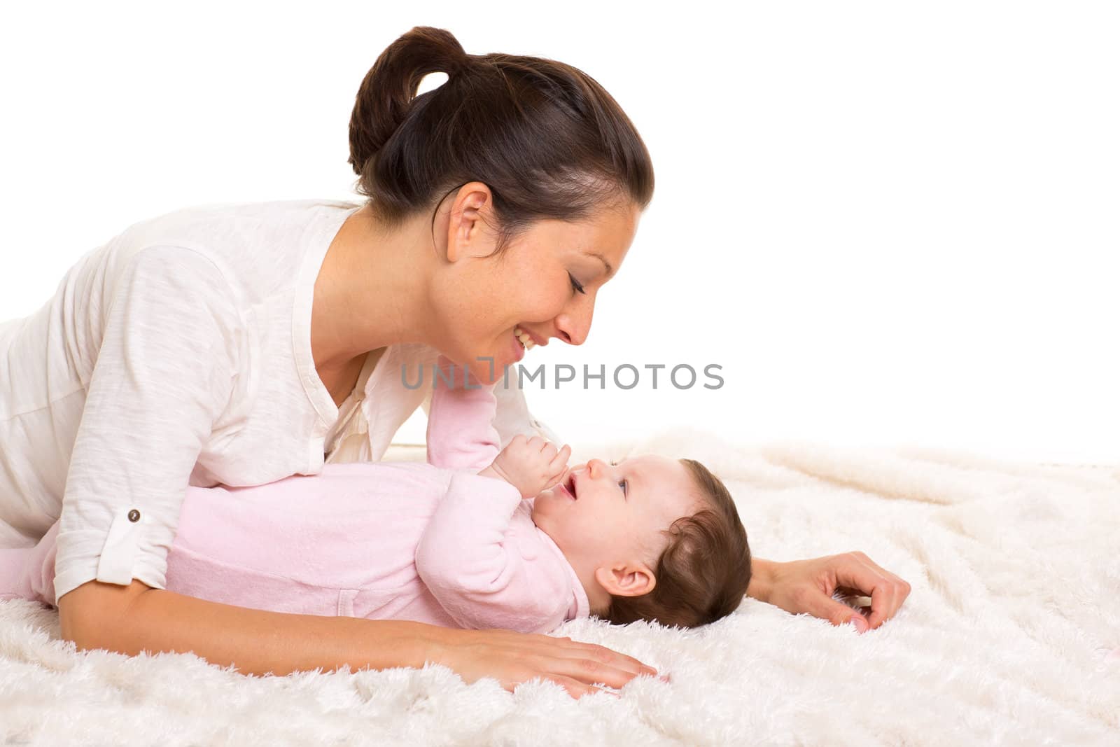 Baby girl and mother lying happy playing together on white fur blanket