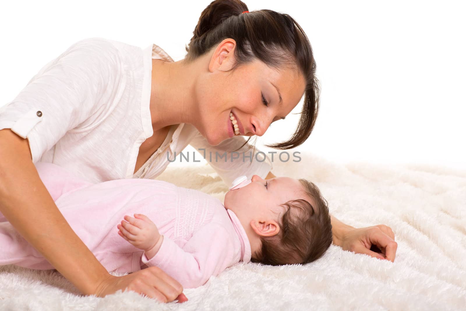 Baby girl and mother lying happy playing together on white fur blanket