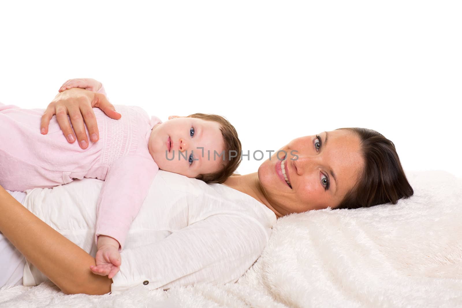 Baby girl and mother lying happy together on white fur blanket