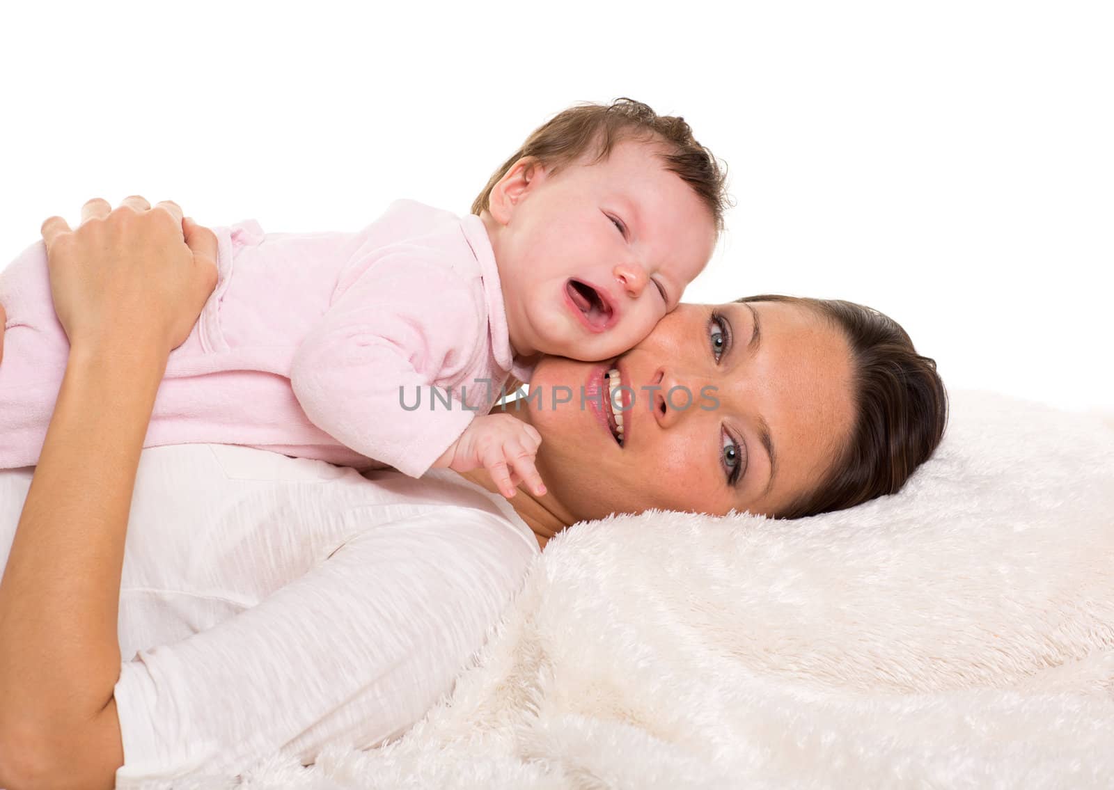 Baby girl crying and mother lying together on white fur by lunamarina