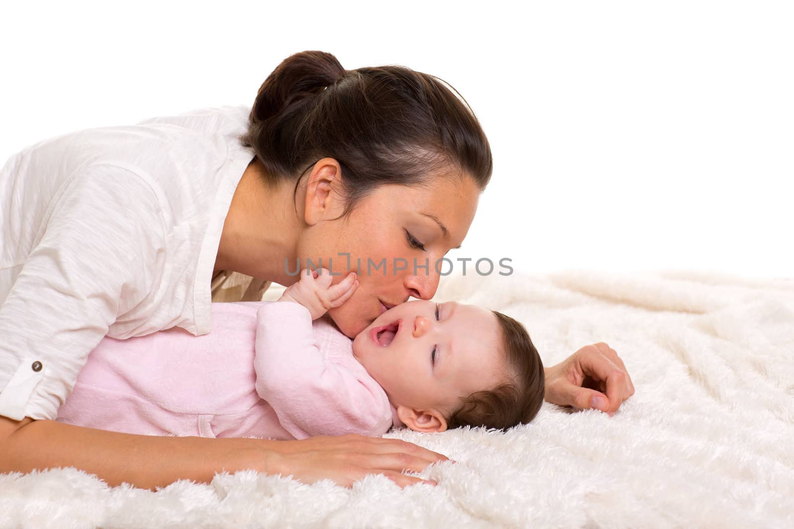 Baby girl and mother kissing her lying happy on white fur blanket