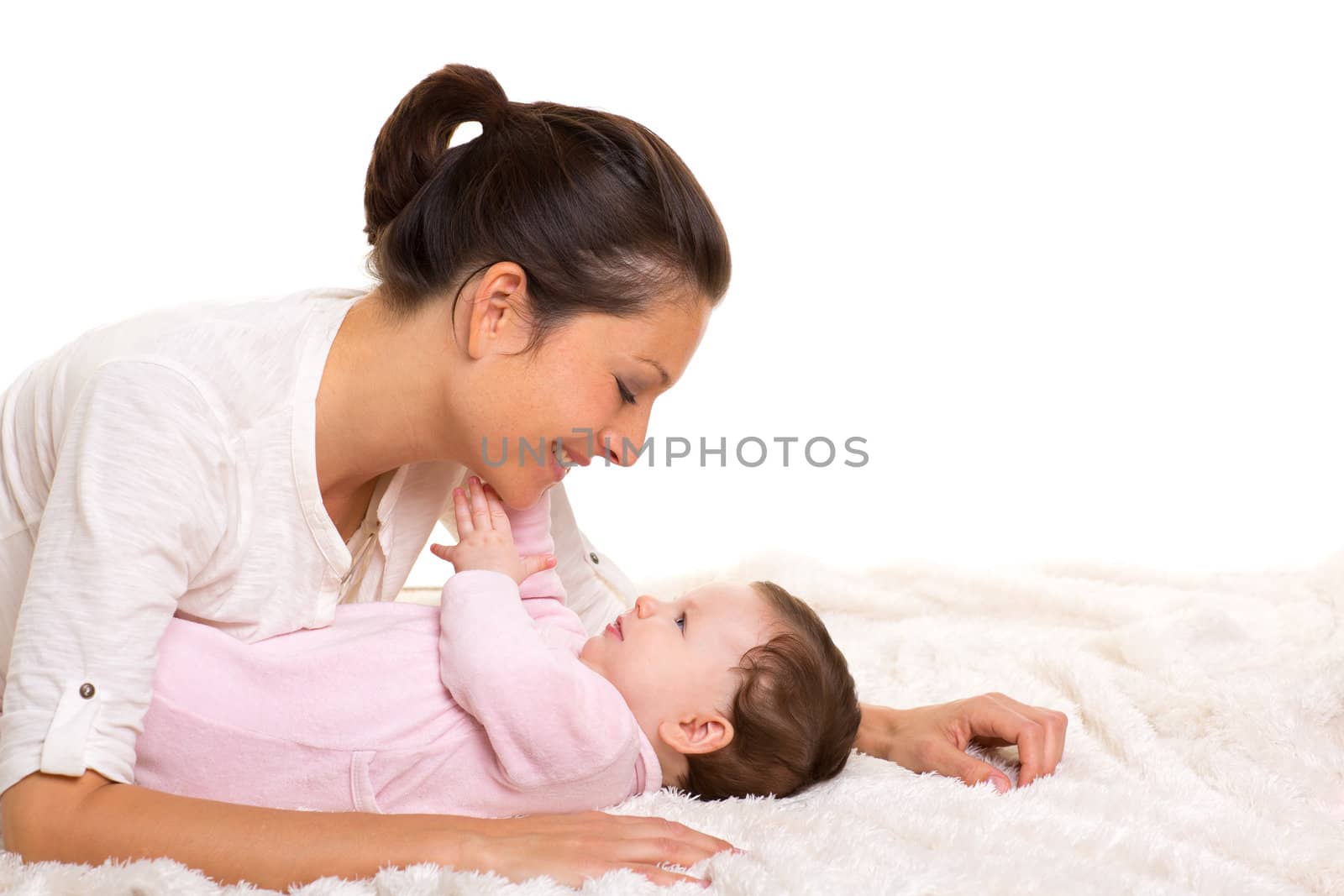 Baby girl and mother lying happy playing together on white fur blanket