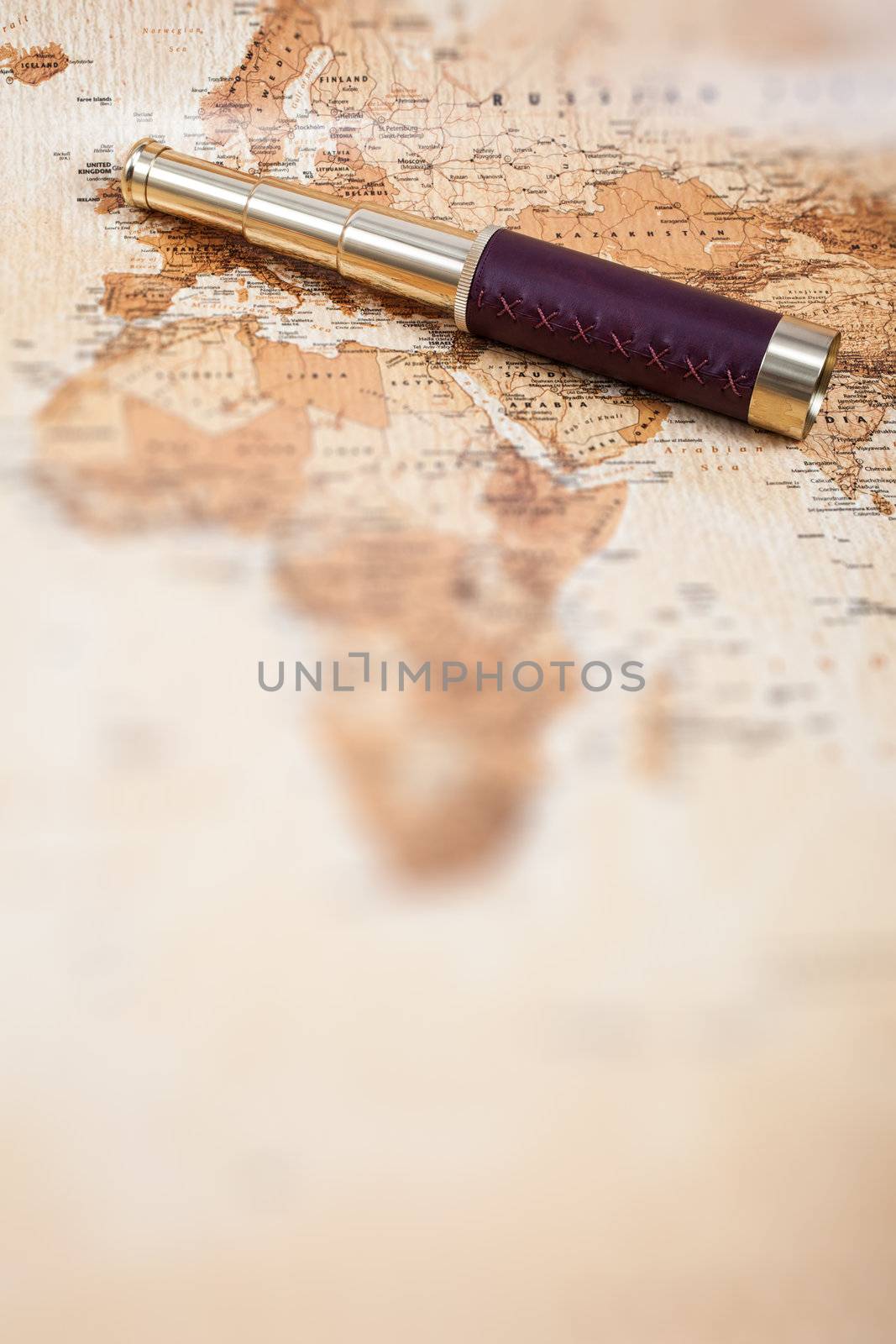 An antique, out of focus, map with a beautiful golden and leather telescope.