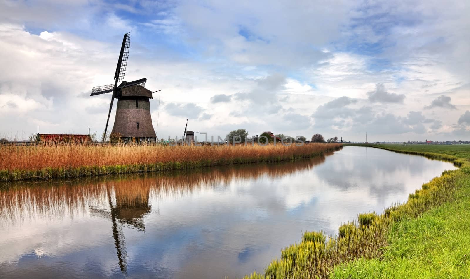 Image of a traditional Dutch windmill near a canal in a cloudy day.