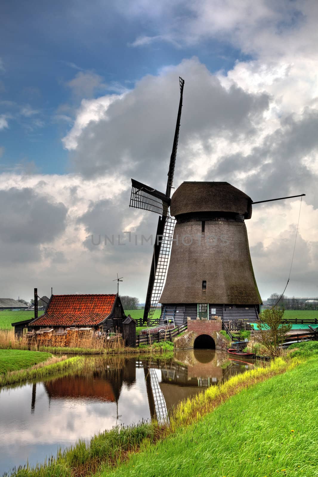 Image of a traditional Dutch windmill near a canal in a cloudy day.