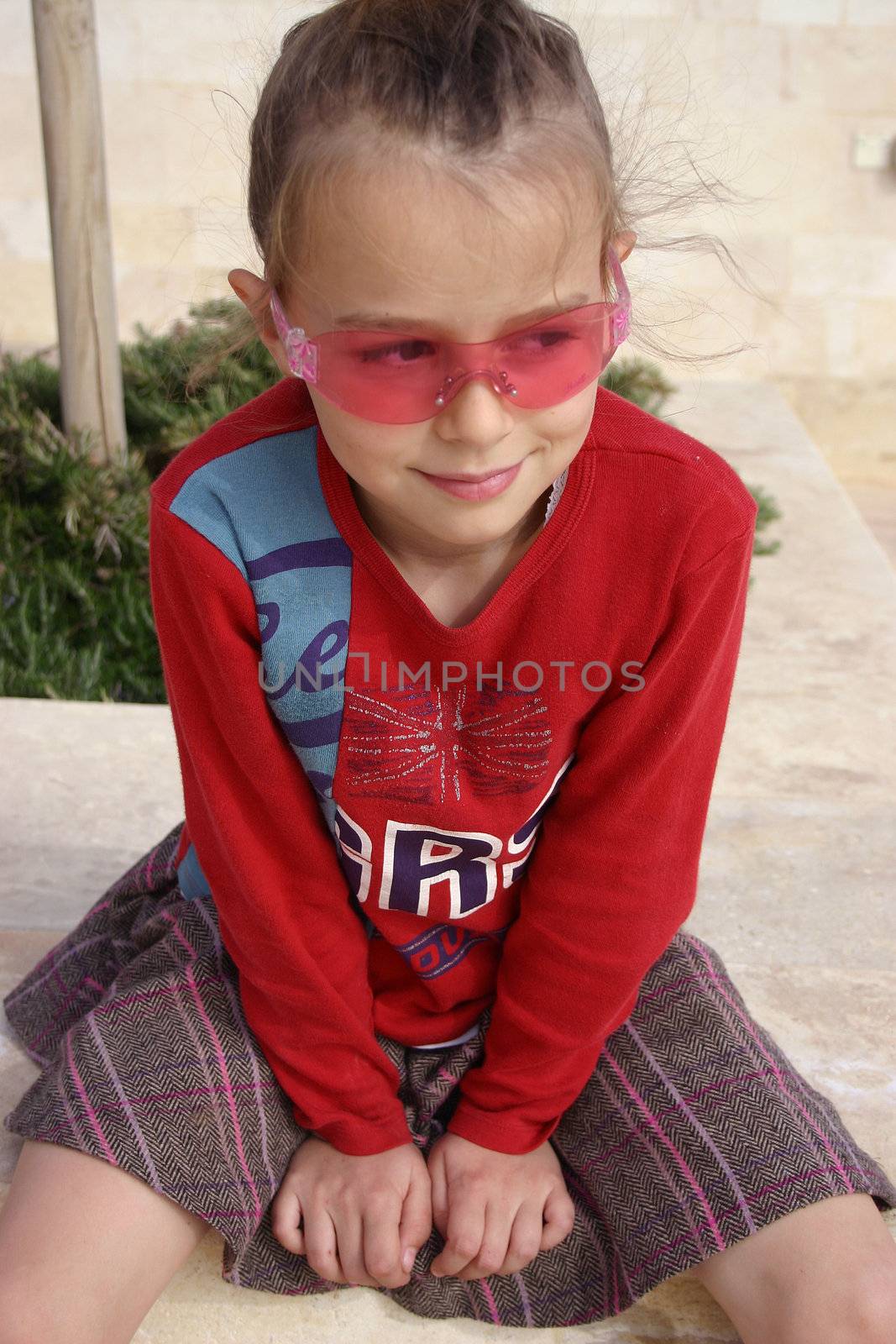 A young girl wearing pink sunglasses, smiling and not looking into the camera