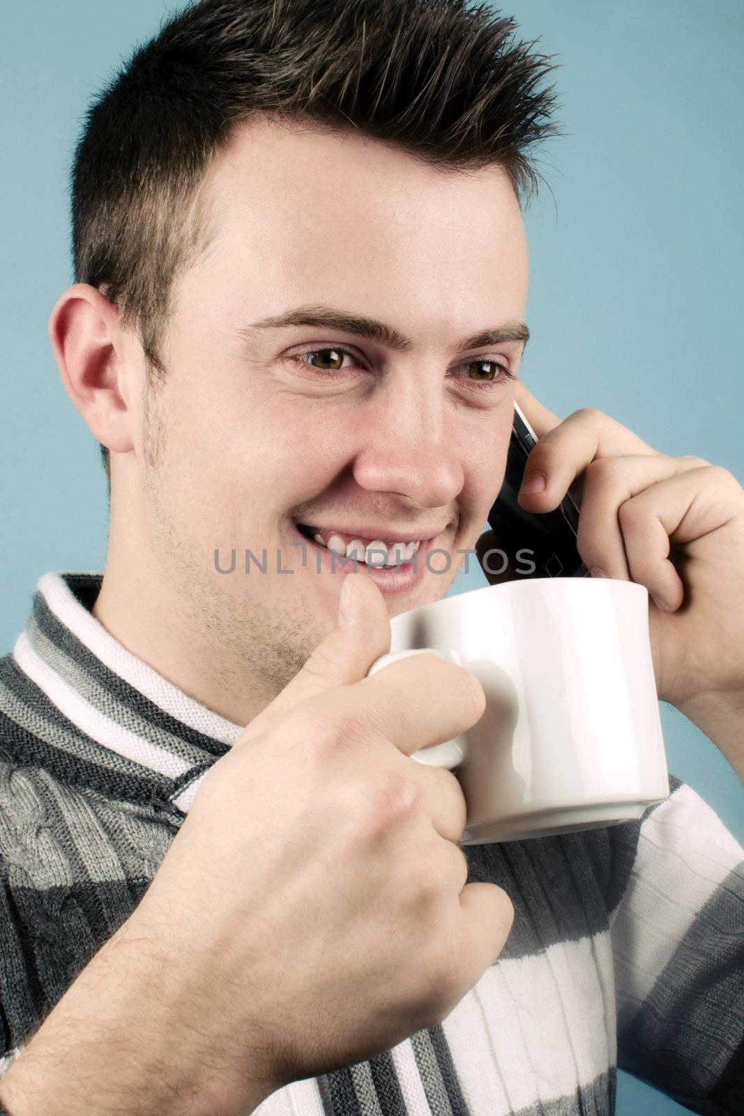 Young man talking on the phone and drinking a hot drink