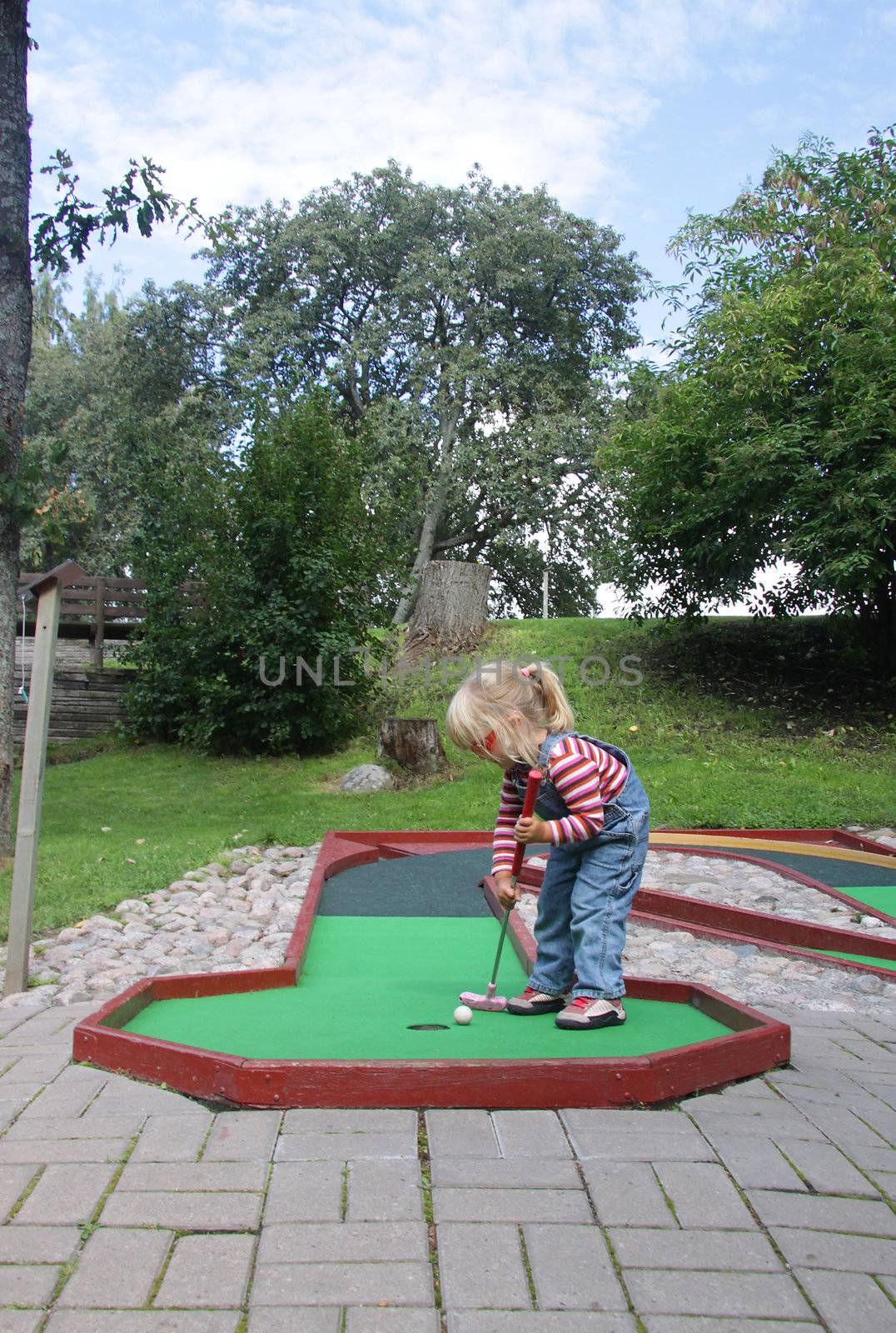 A little cute girl putting a ball when playing minitiature golf