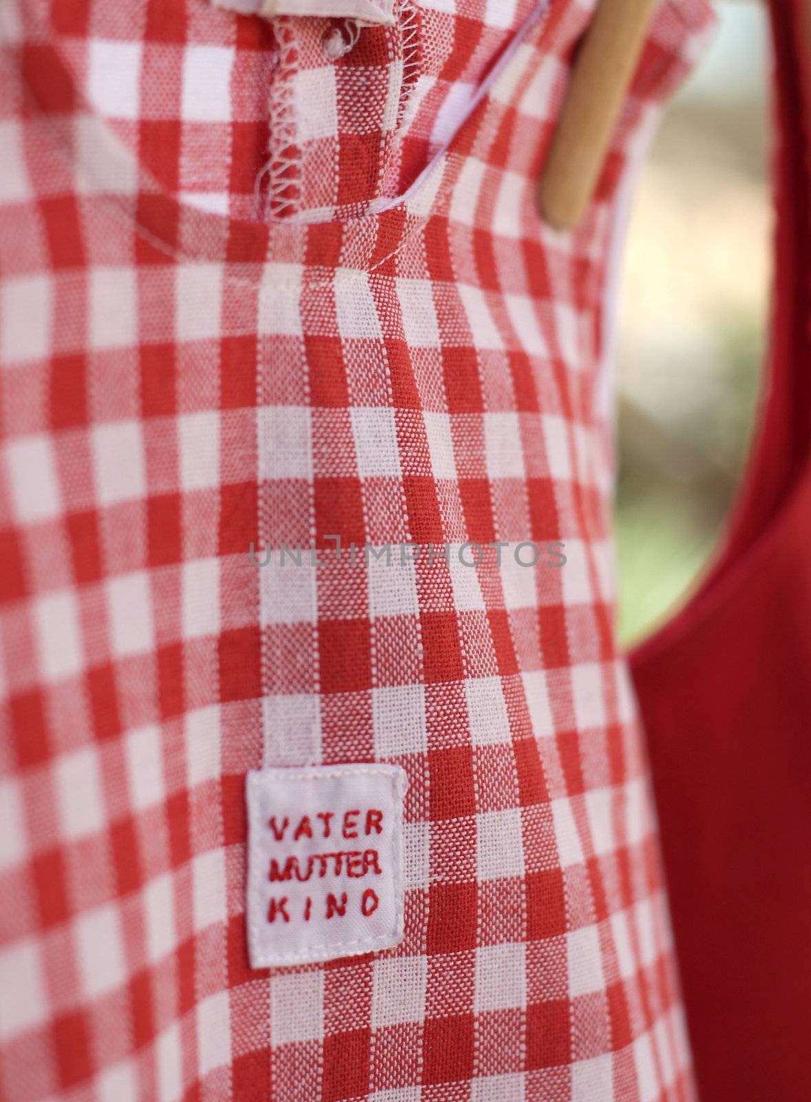 White and red chequed baby dress pegged up with wooden pegs on a clothes line. The label reads Vater, Mutter, Kinder which means Father, Mother, Child in German