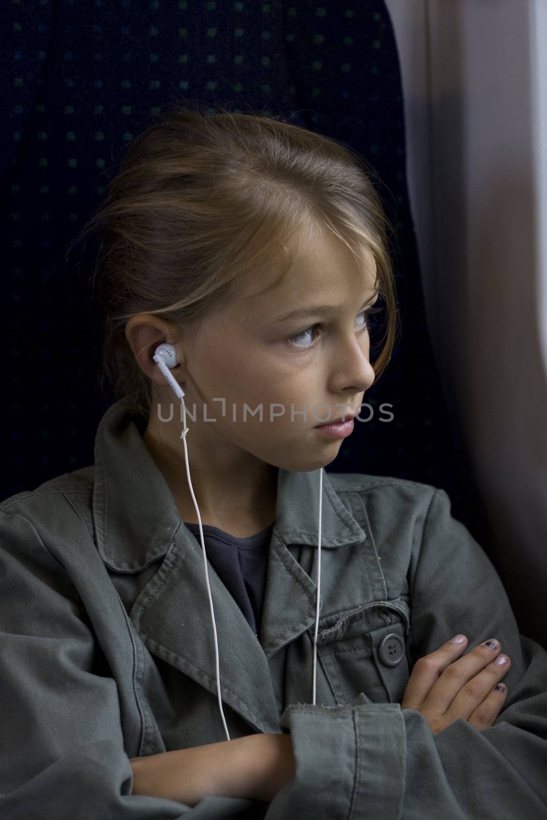 A young girl with headset sitting on a train, looking out of the window. 