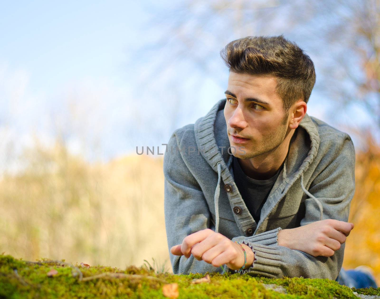 Handsome young man outdoors in nature lying on moss, large copyspace