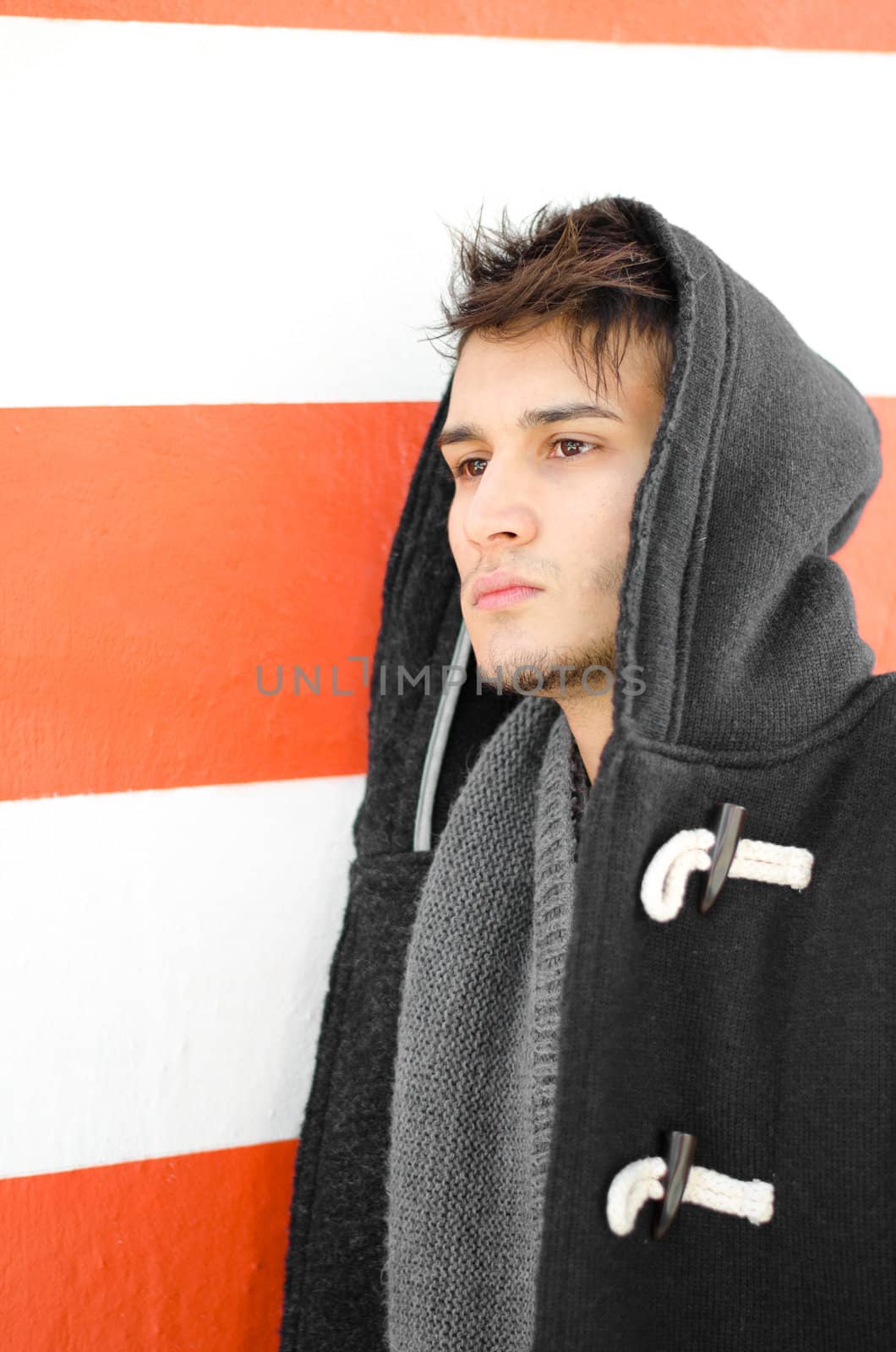 Attractive young man in hoodie against white and orange striped wall