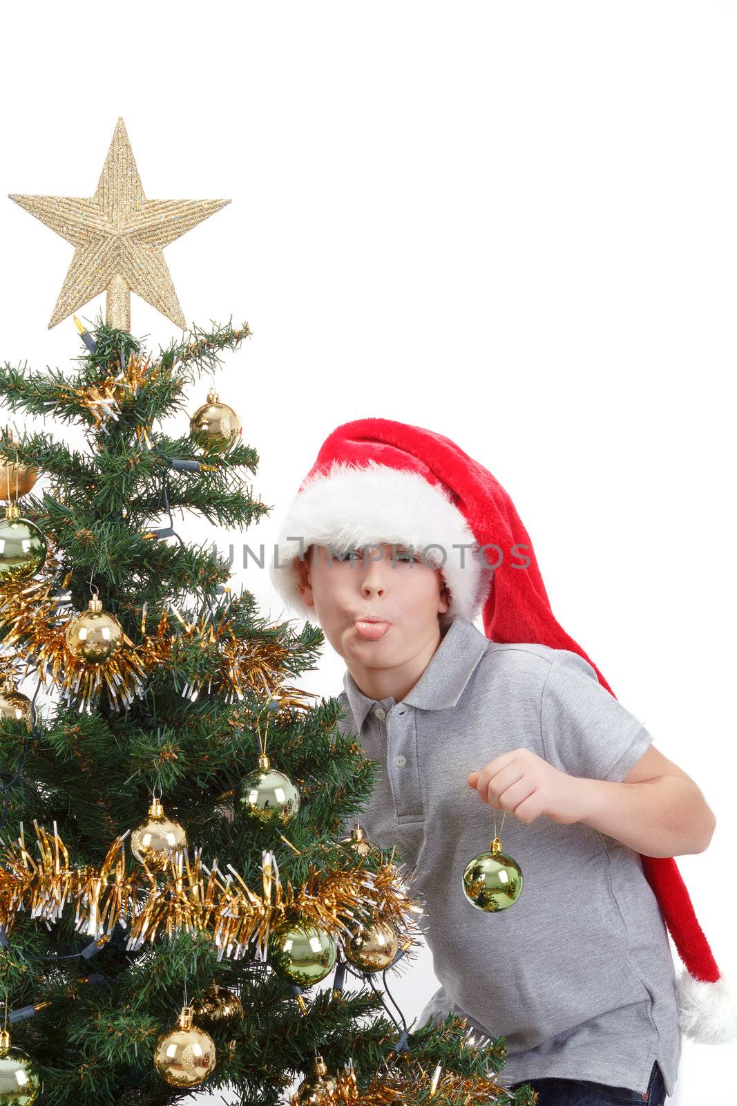 Boy with santa hat sticking out tongue at  the Christmas tree on white background