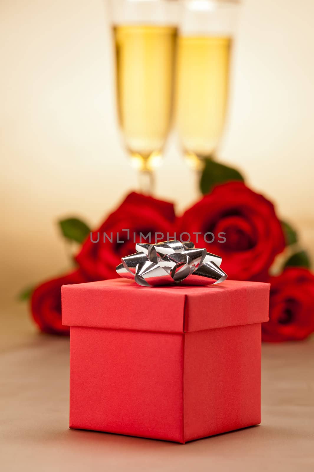 Champagne glasses, present and roses in front of beige background