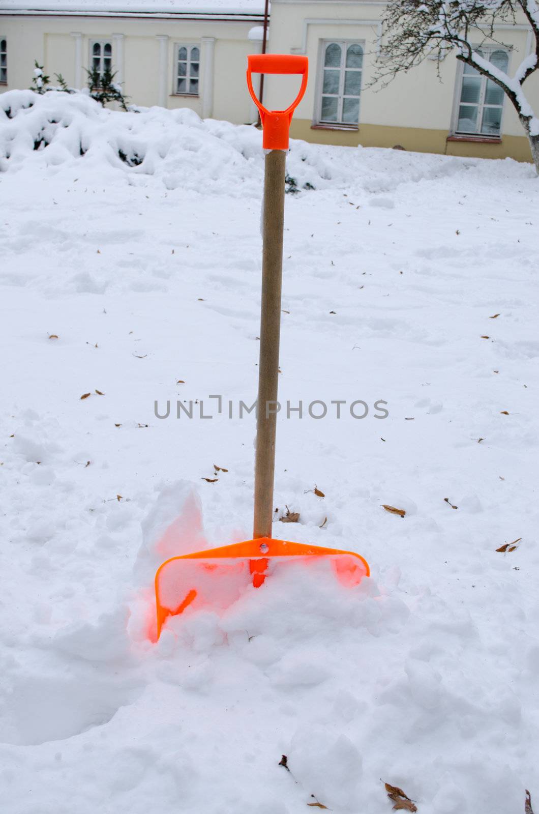 orange plastic snow clean tool in winter snowdrift snow heap and house in background.