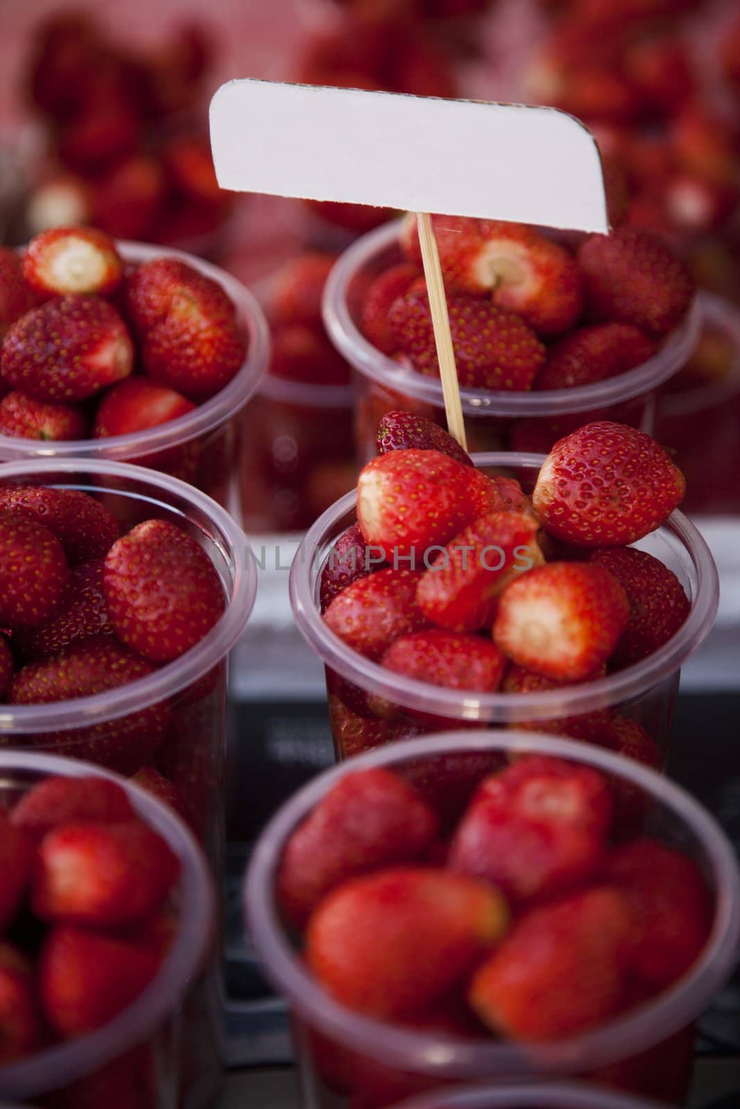 Strawberries in plastic cups on sale  at market with empty label