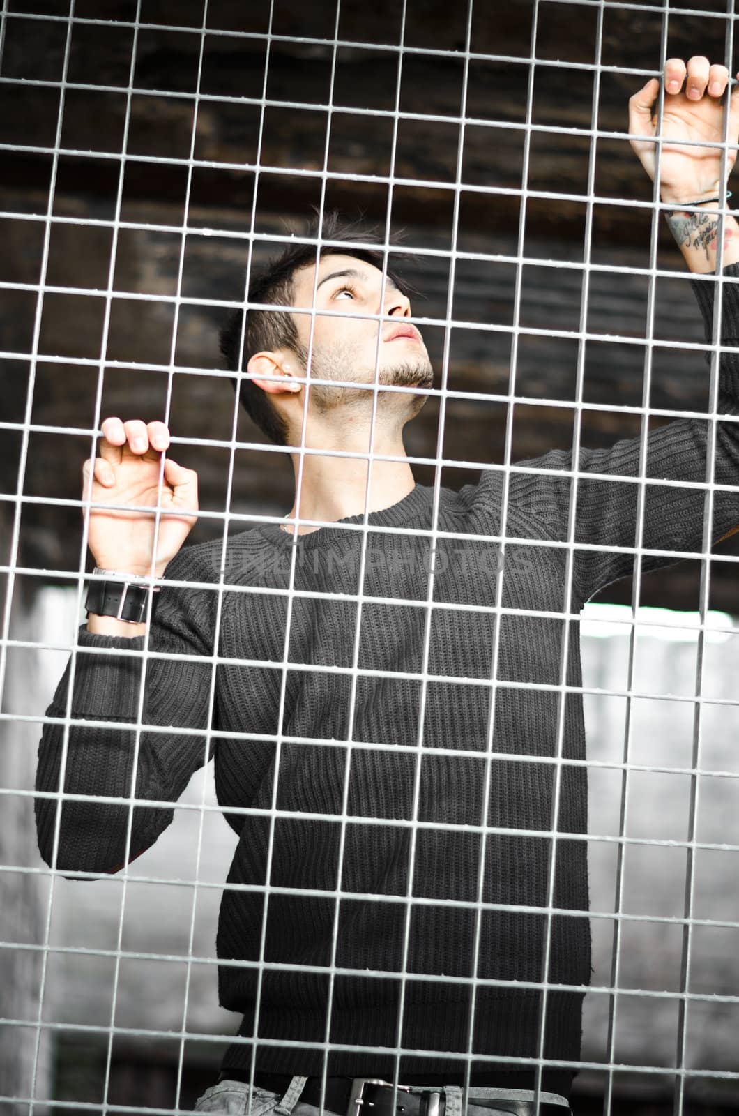 Attractive young man behind metal or steel net by artofphoto