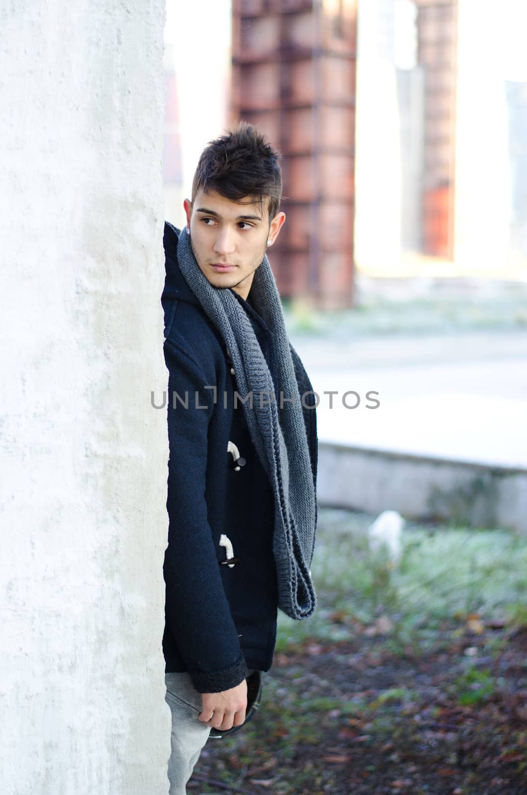 Handsome young man standing behind white wall and looking over it