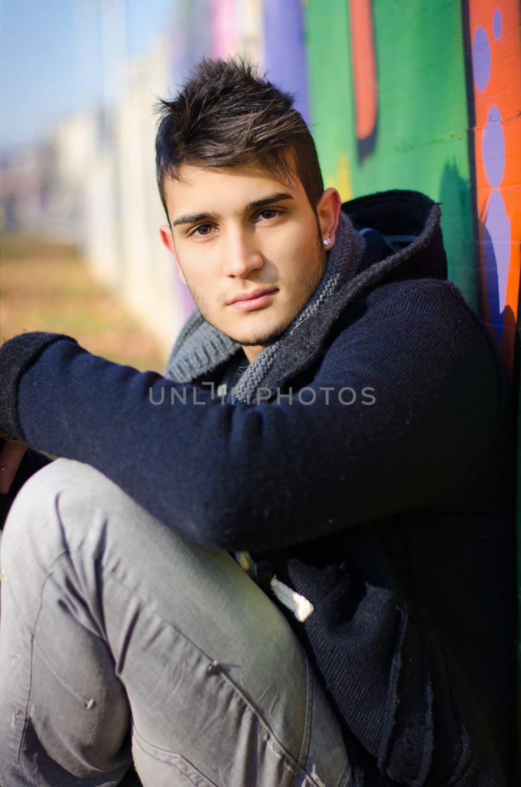 Handsome young man sitting against colorful graffiti by artofphoto