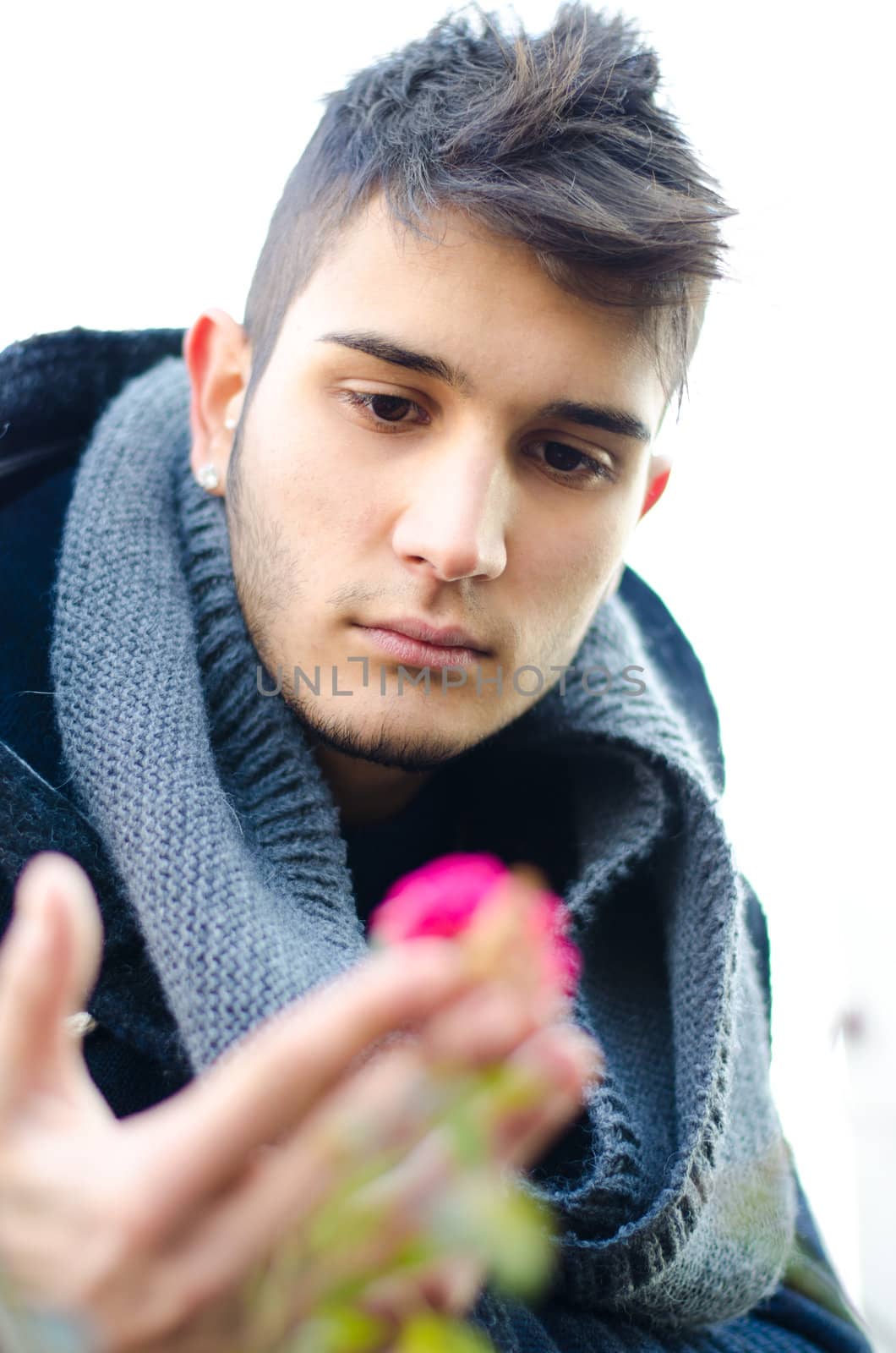 Handsome young man holding and looking at a purple flower