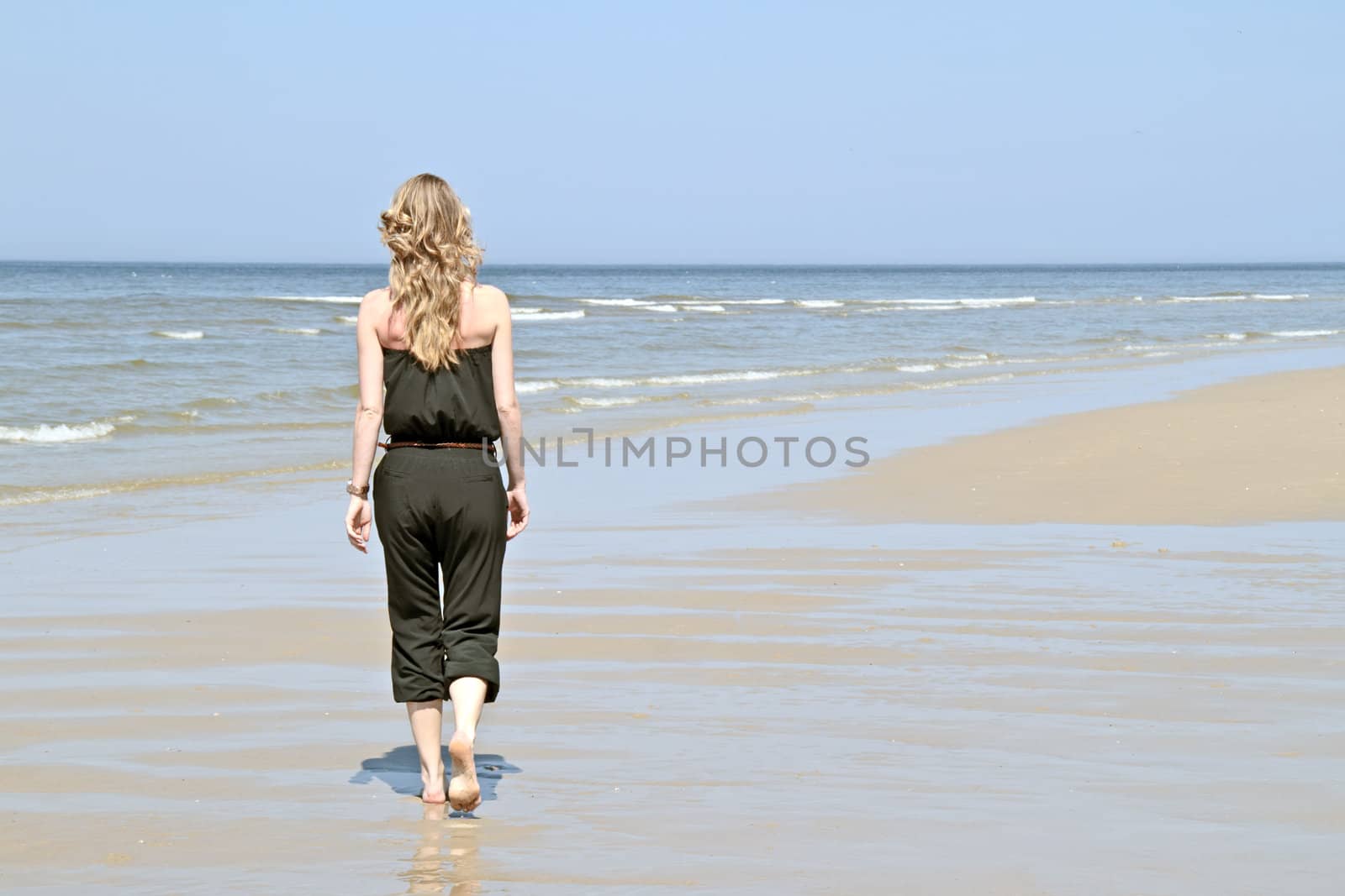 Beautiful young blonde woman walking along the beach
