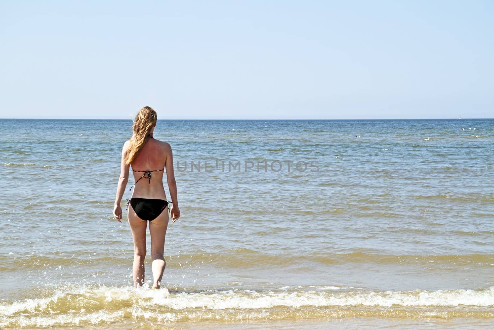 Young blonde woman walking into the ocean  by devy